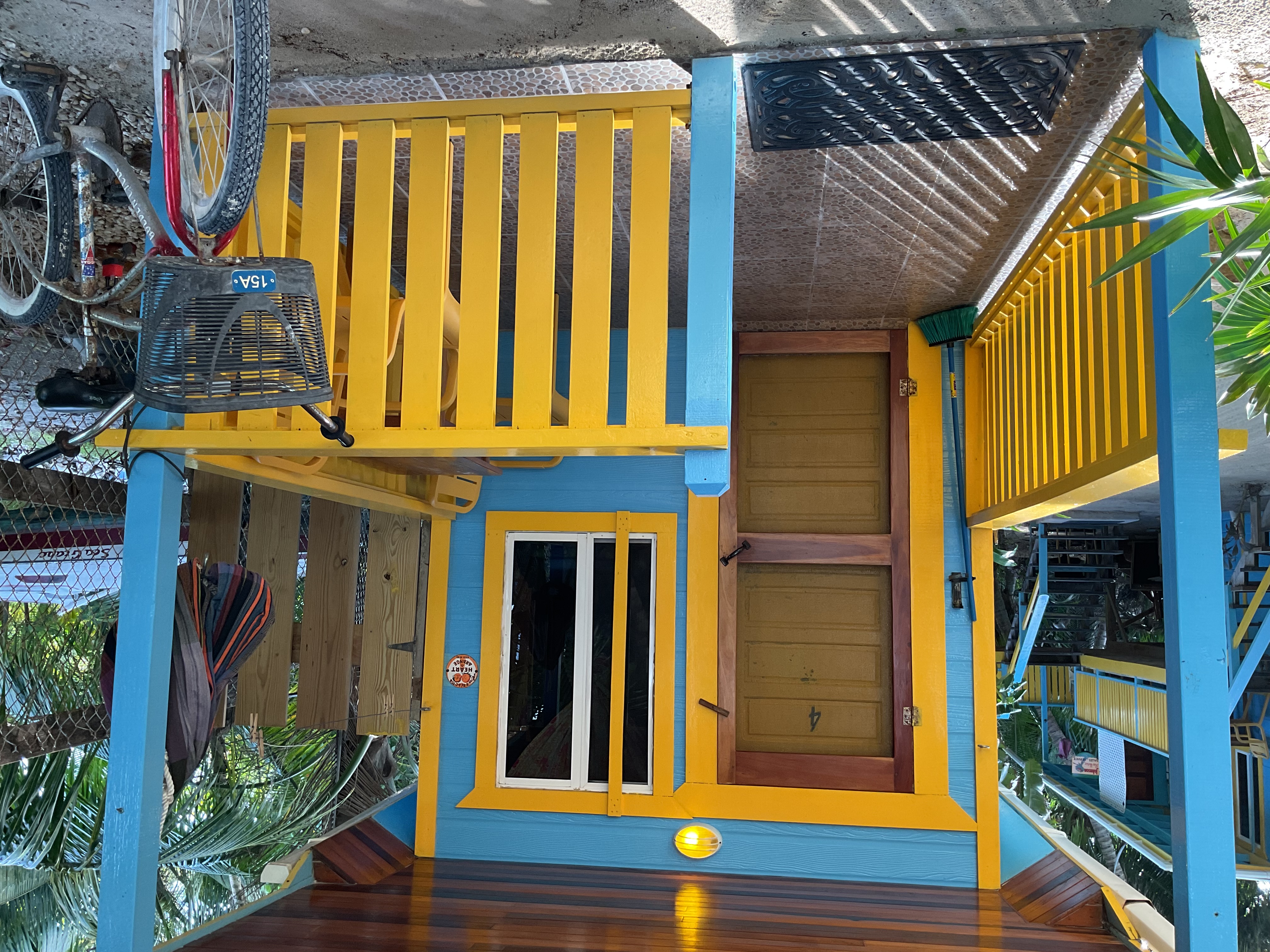 Bird's eye view of cheerfully painted blue and yellow ground-level tiny house surrounded by sand and palm trees