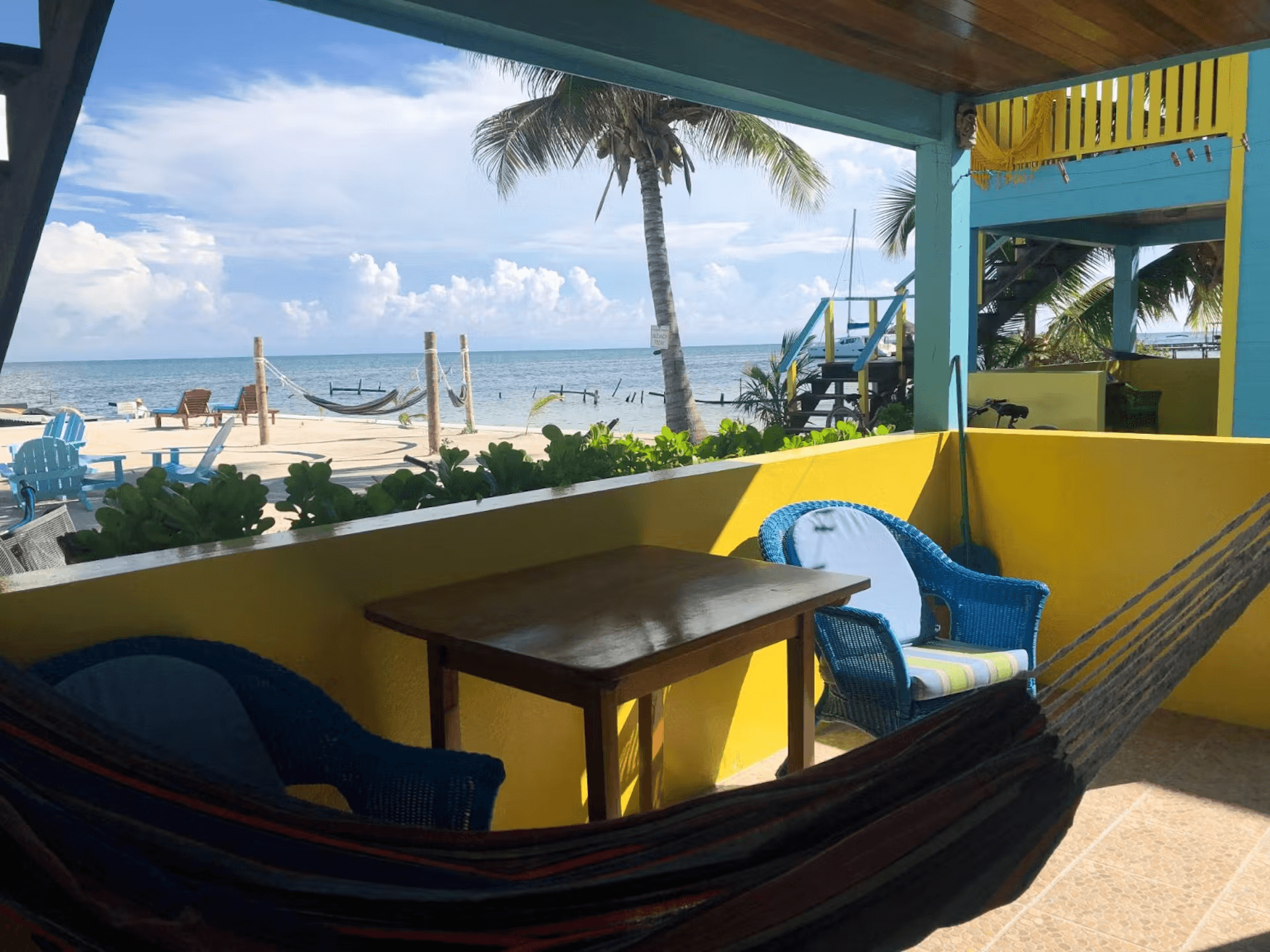 Brightly painted blue and yellow porch with hammock and wicker chairs with beach views