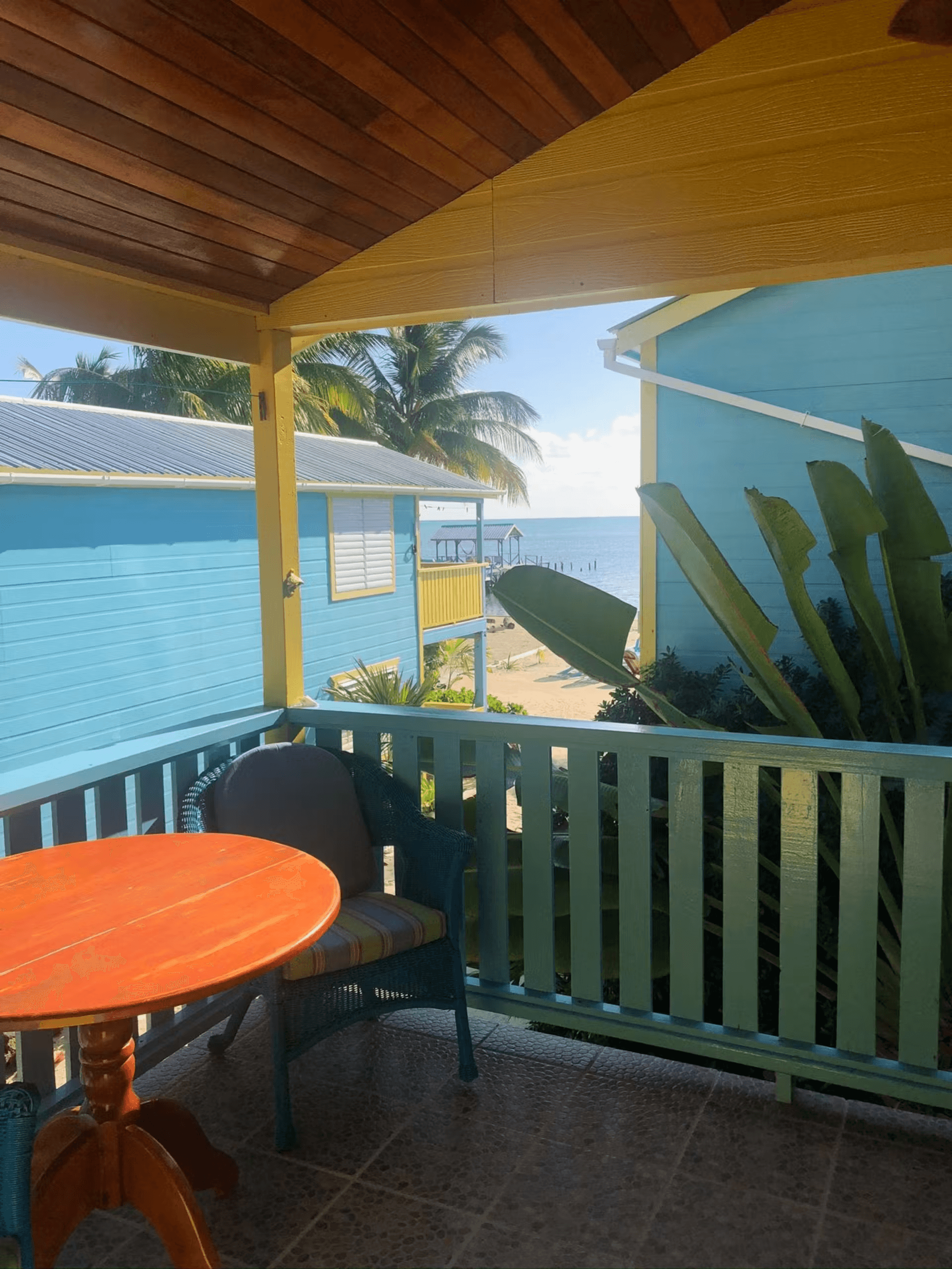 Balcony with cushioned chair and round table, view shows two other cabanas with the beach and ocean beyond