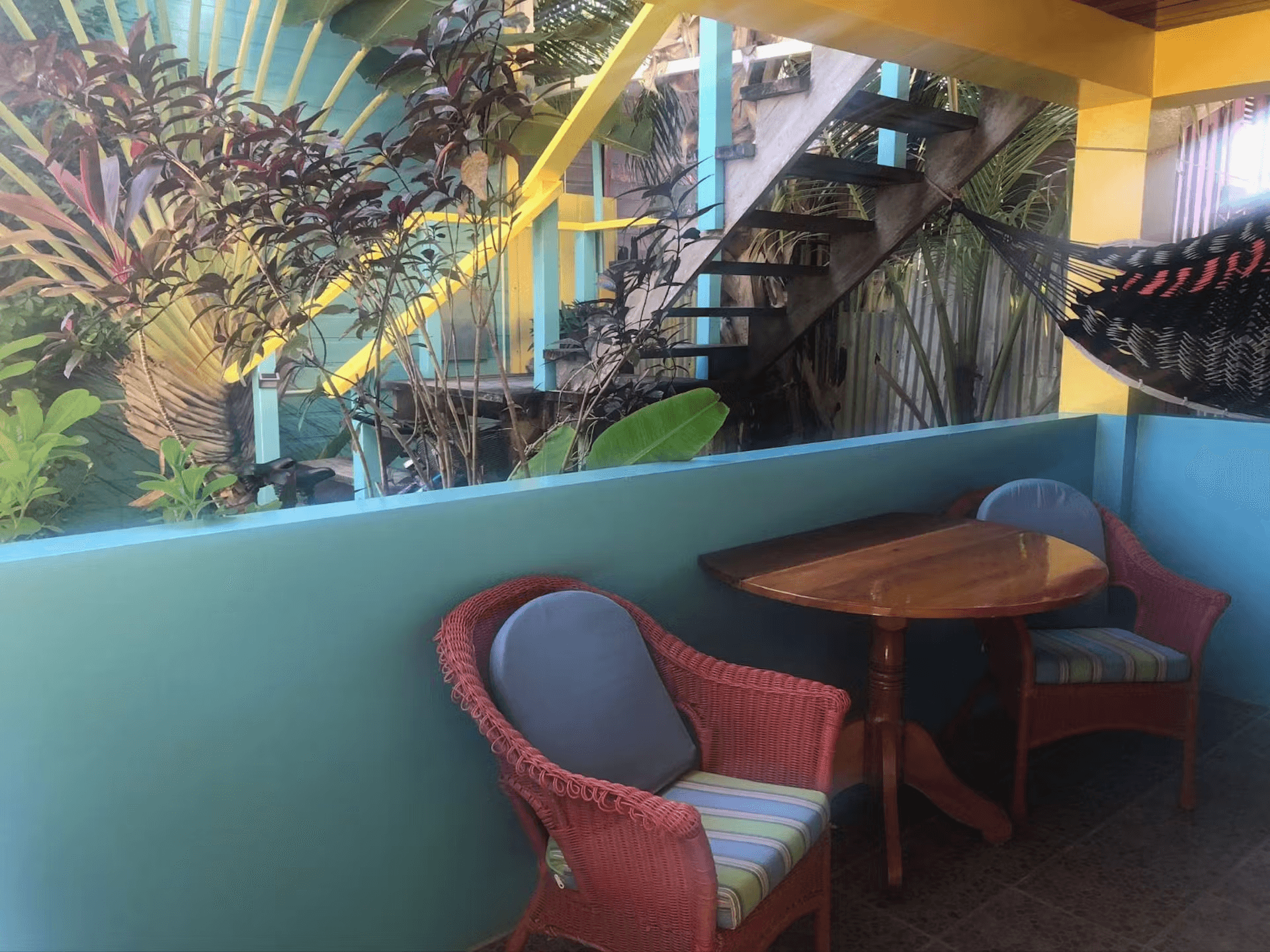 Patio with two chairs, a table, and a hammock with lush tropical foliage behind