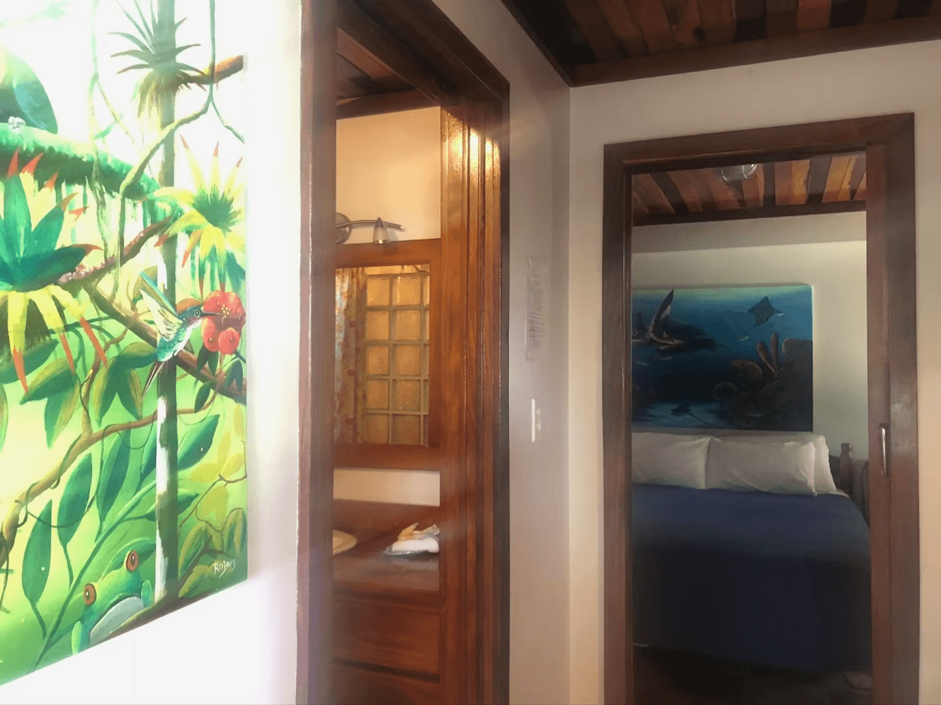 View of doorways leading into the bathroom and the bedroom, brightly colored tropical artwork hangs on the wall