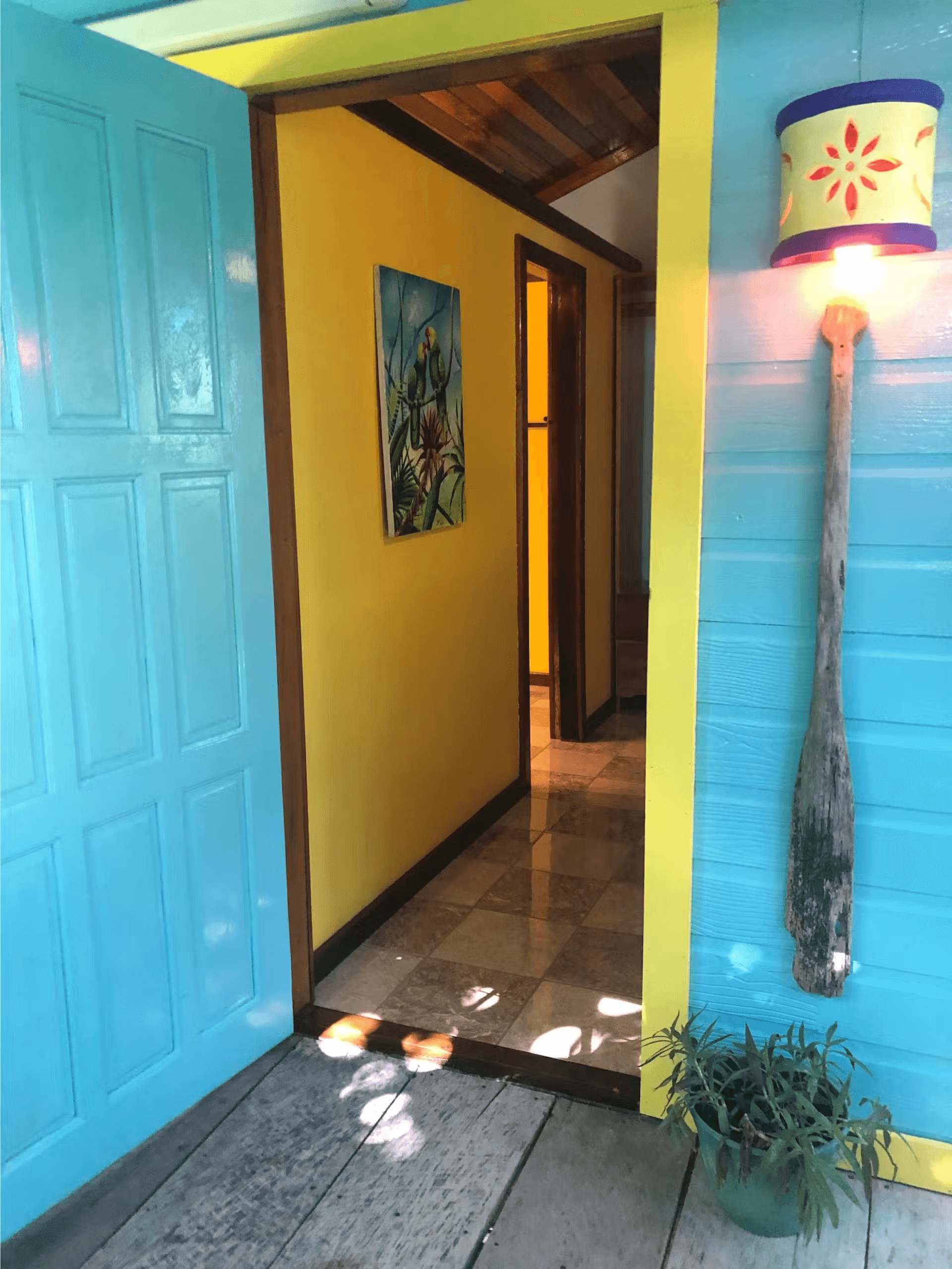 Bright blue front door leading into living area of cabana, the right side of the doorway is adorned with a decorative light, a paddle, and a potted plant