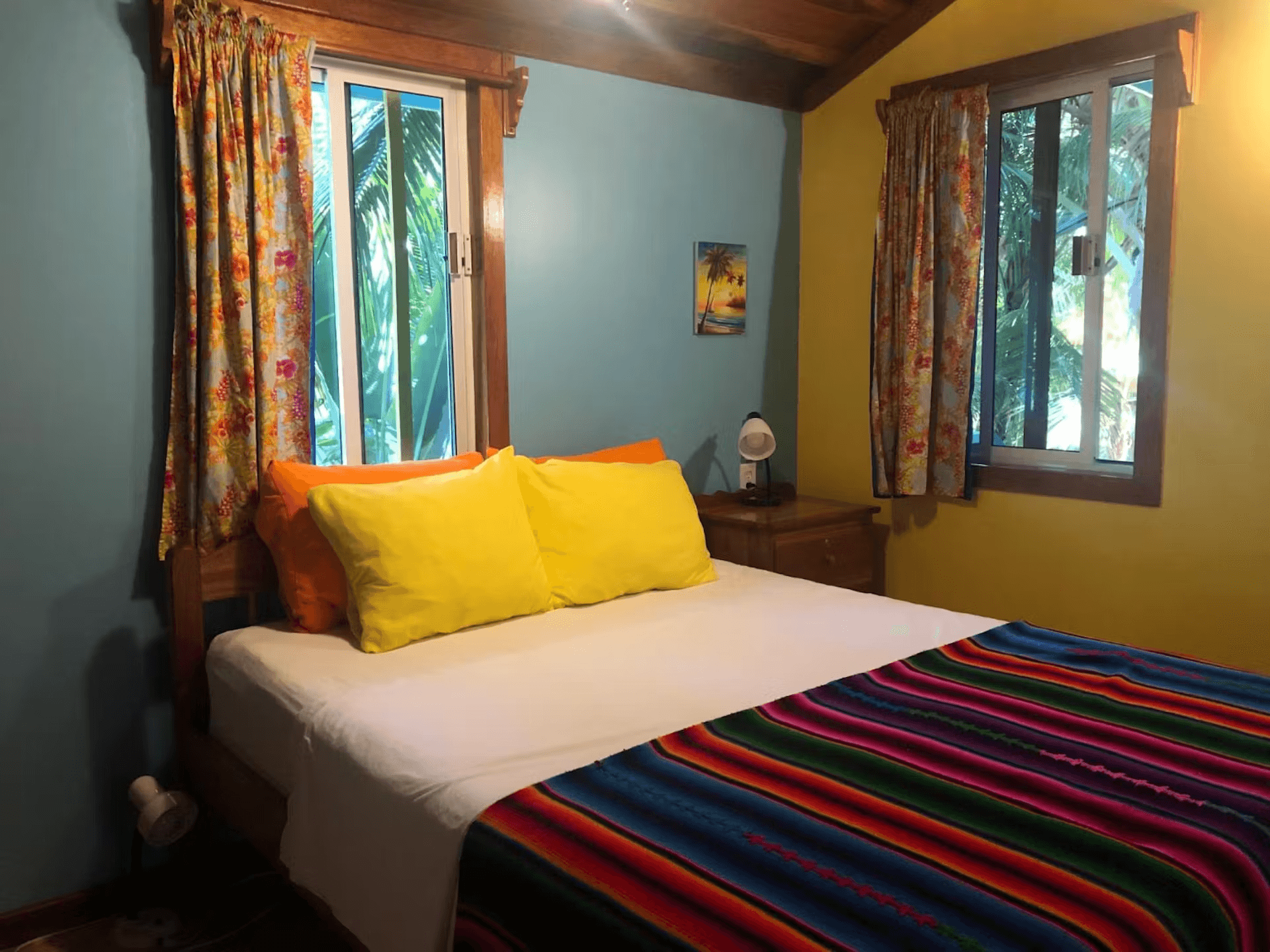 Bedroom painted in blue and yellow, a queen with bright striped bedspread and coordinating pillows