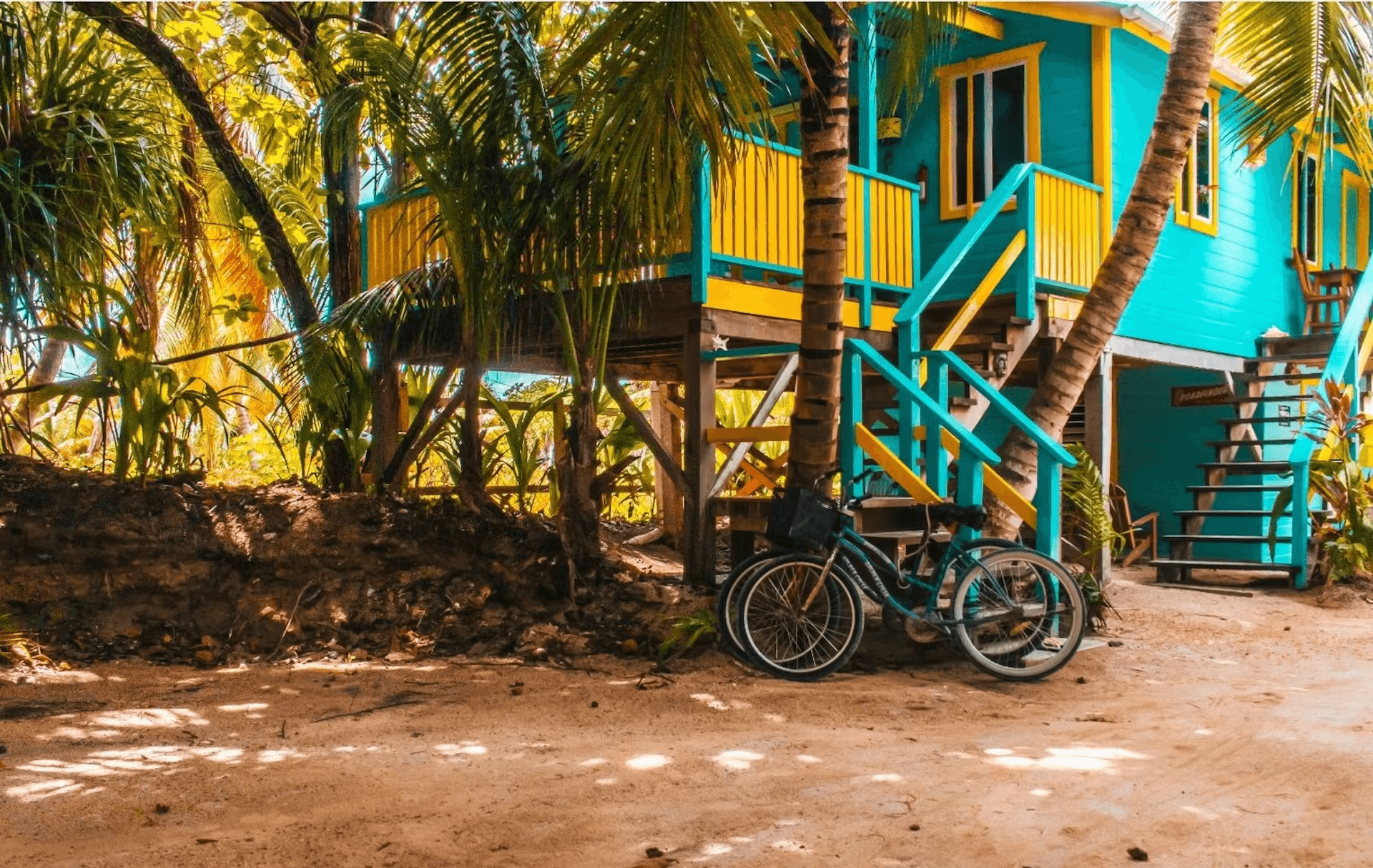 Ground view of a brightly painted blue and white cabana with bicycle leaning against base of stairs leading to second floor