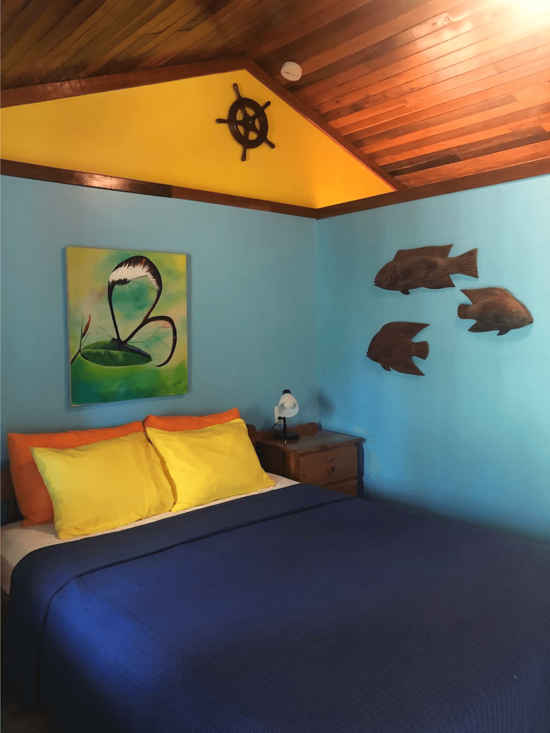 Bedroom decorated in shades of blue and yellow with queen bed, vaulted wood ceilings, three wooden decorative fish on wall