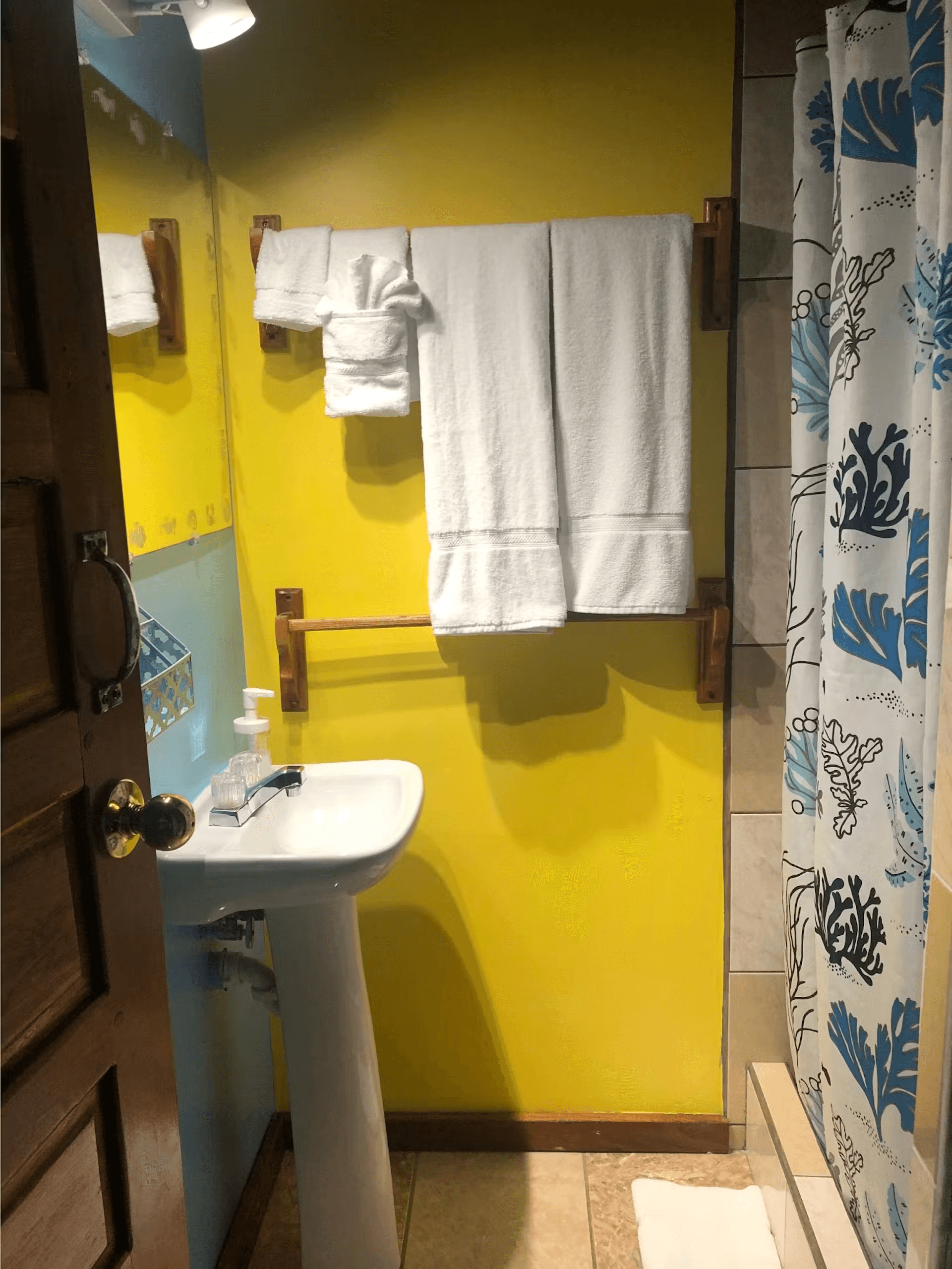 Bathroom with white pedestal sink, tiled shower, and plush white towels hanging on wall