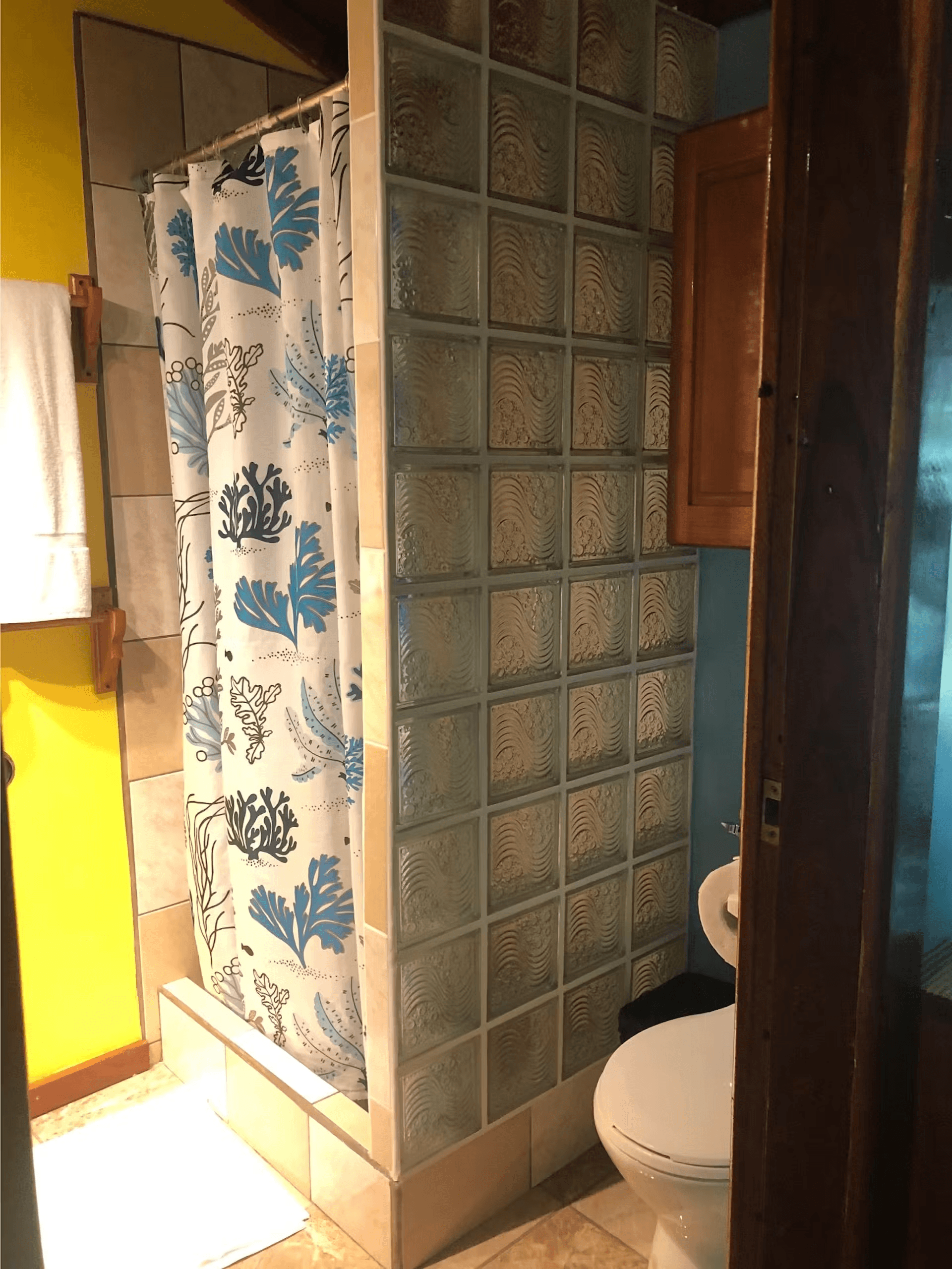 Tiled shower next to toilet with plush white towels hanging on bright yellow wall