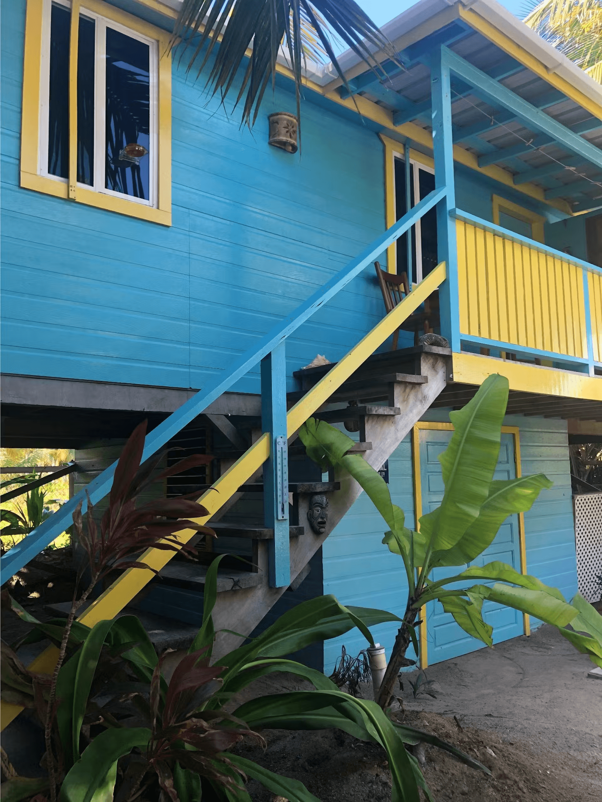 Exterior of brightly painted blue and yellow cabana with stairs leading to balcony