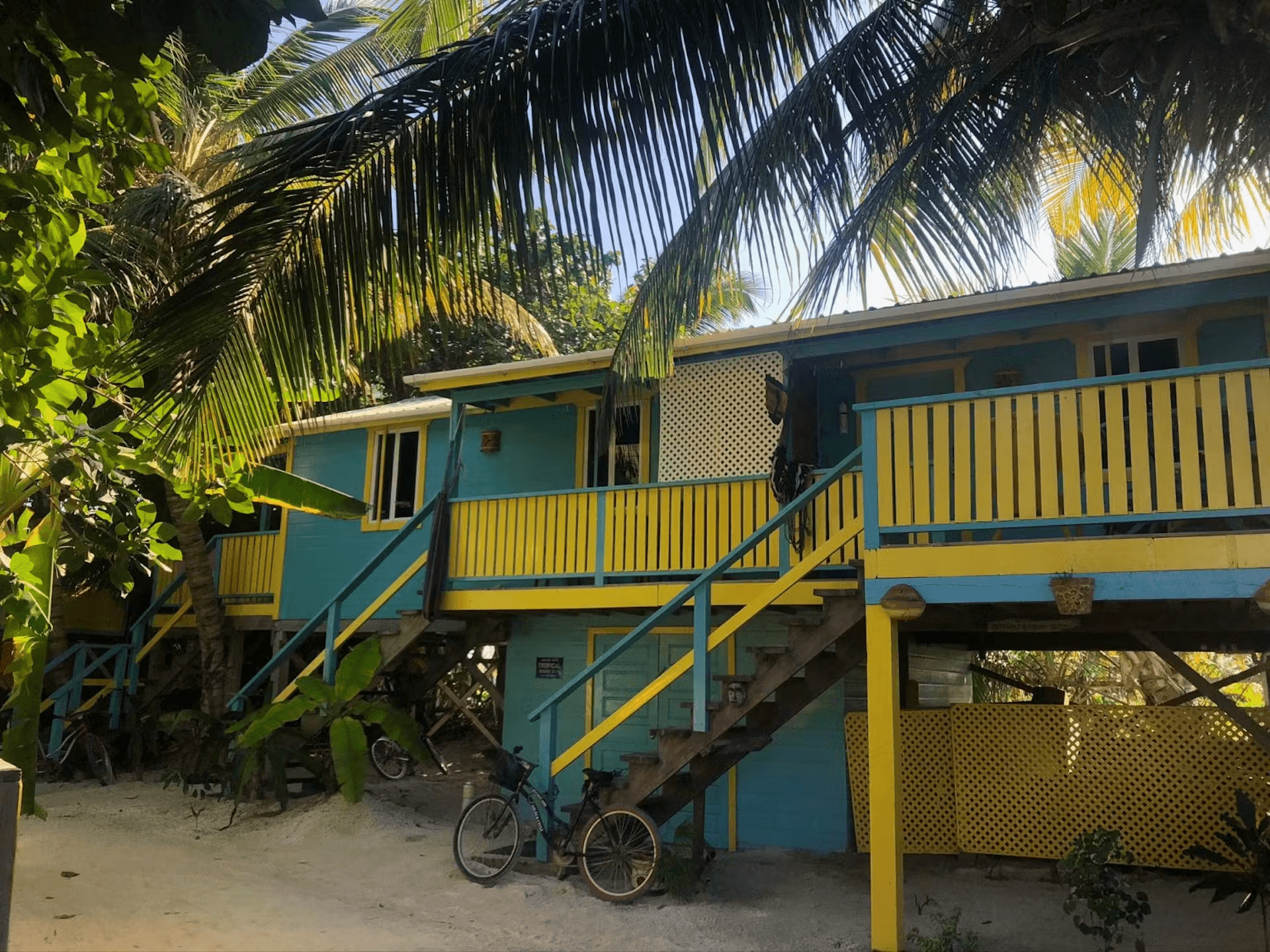 Exterior of a colorful blue and yellow cabana with stairs leading to second level, framed by tropical foliage
