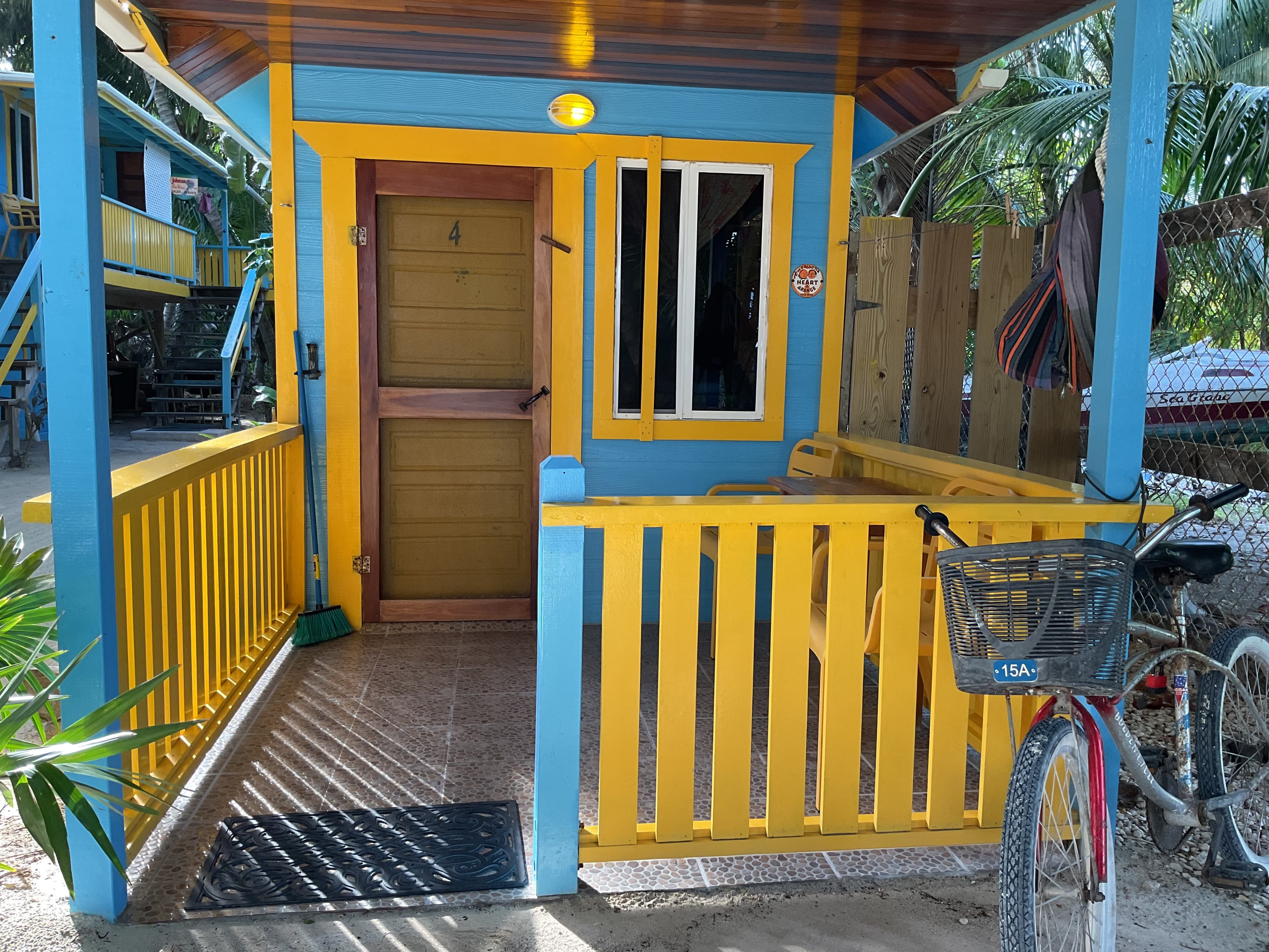 Bird's eye view of cheerfully painted blue and yellow ground-level tiny house surrounded by sand and palm trees