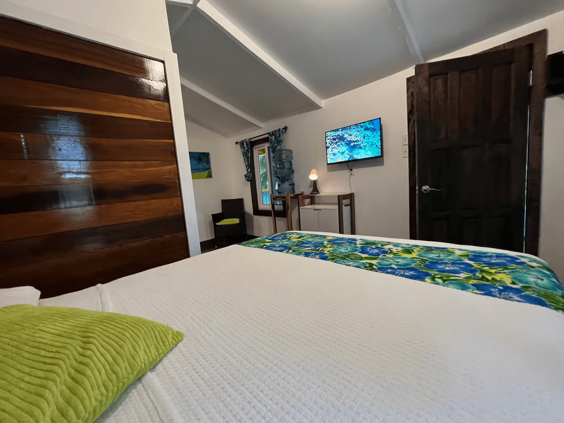 View from bed showing Belizean hardwood accents, wall-mounted TV, and side table with chair
