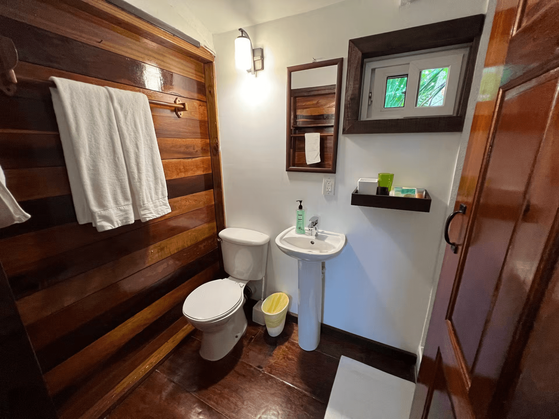 Bathroom with pedestal sink, toilet, and plush white towels hanging on wall of Belizean hardwood
