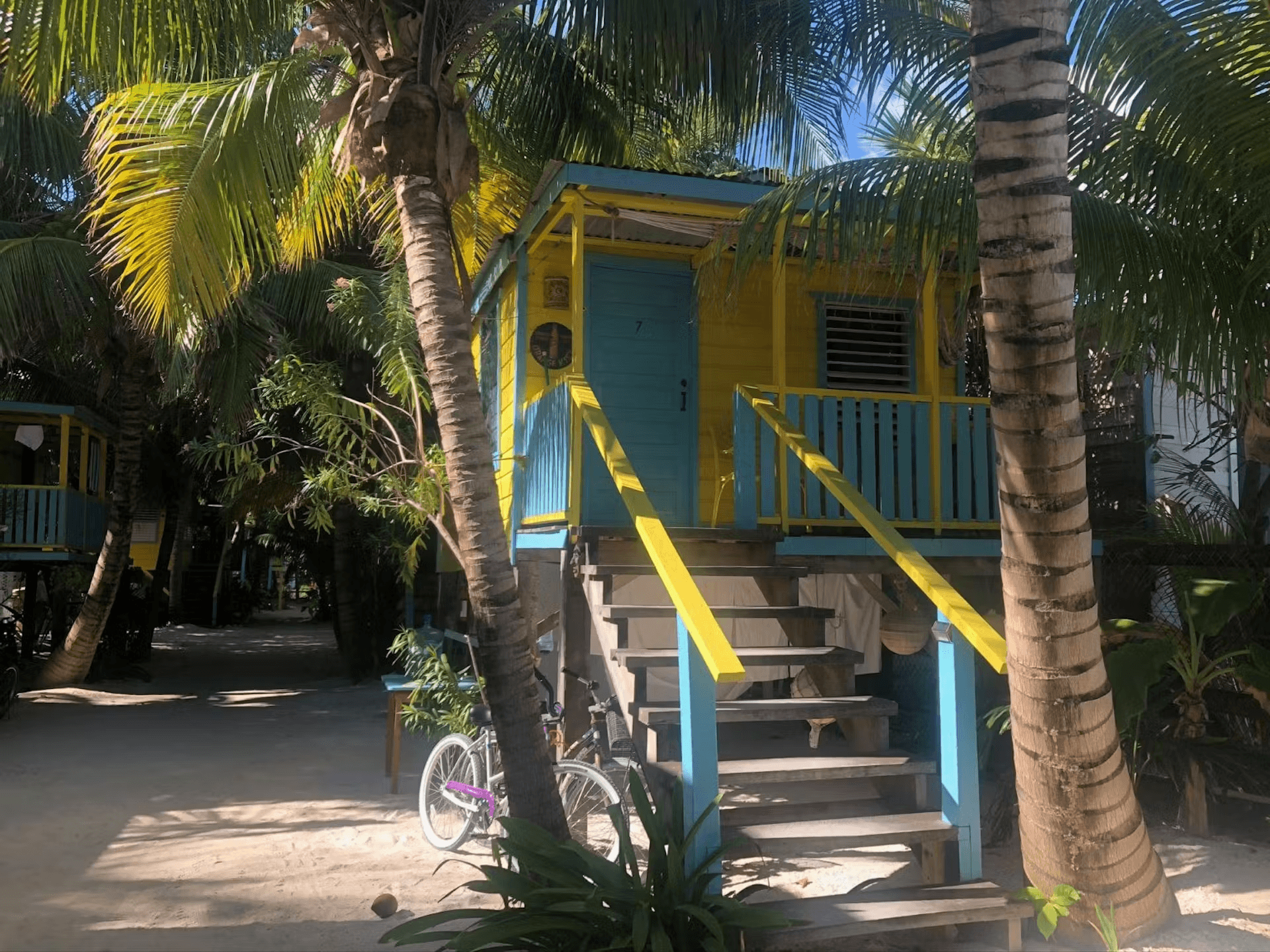 Exterior of a colorful blue and yellow cabana with stairs leading to second level and palm trees flanking steps