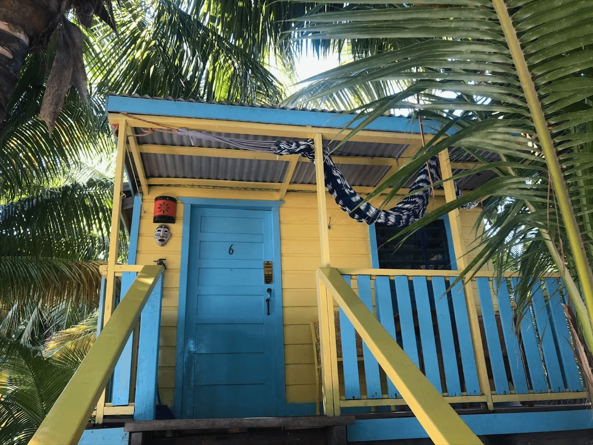 View looking up at front door and balcony of bright blue and yellow painted cabana