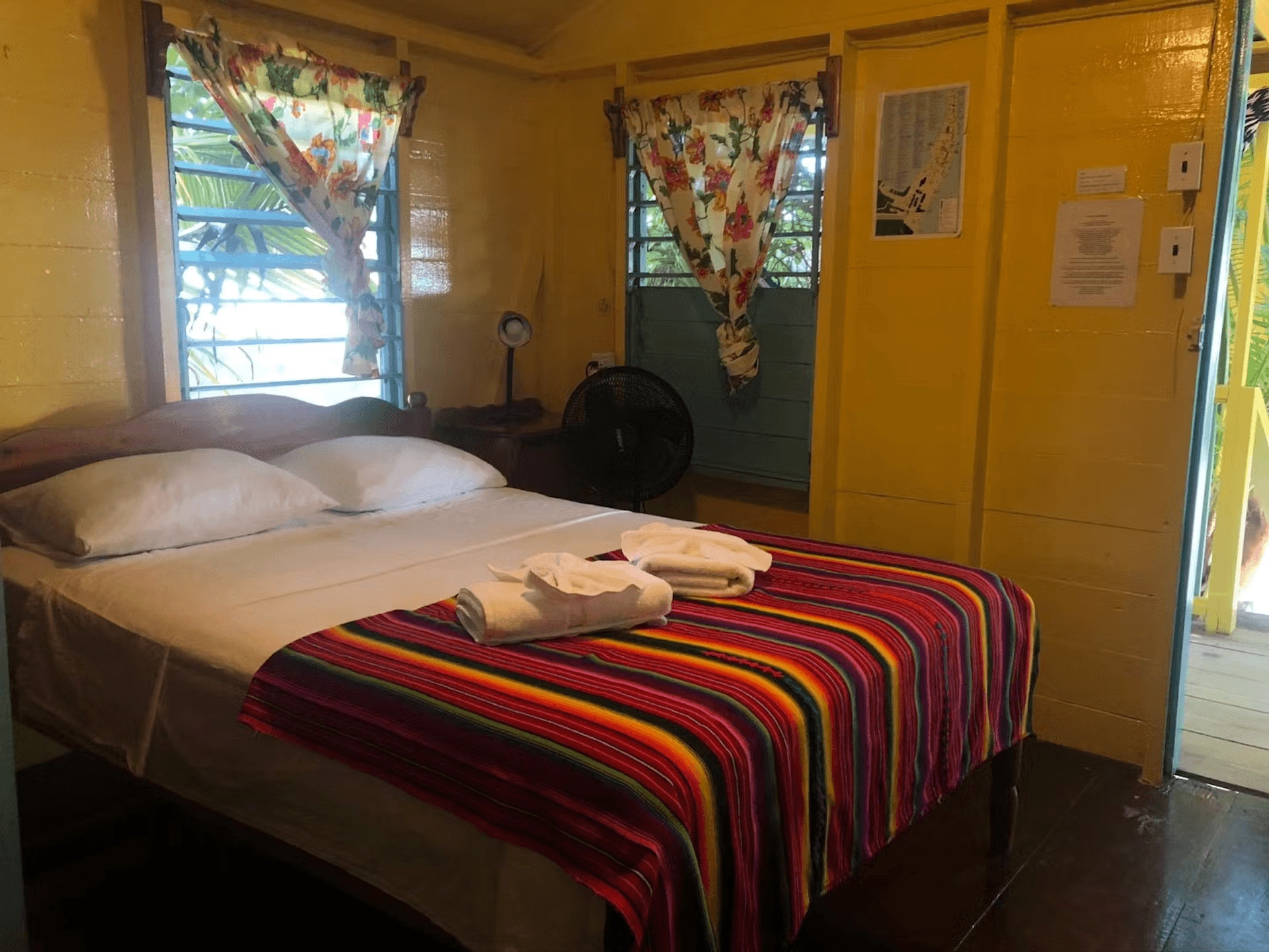 Bedroom with bright yellow walls, sunny windows, double bed, and doorway leading to balcony