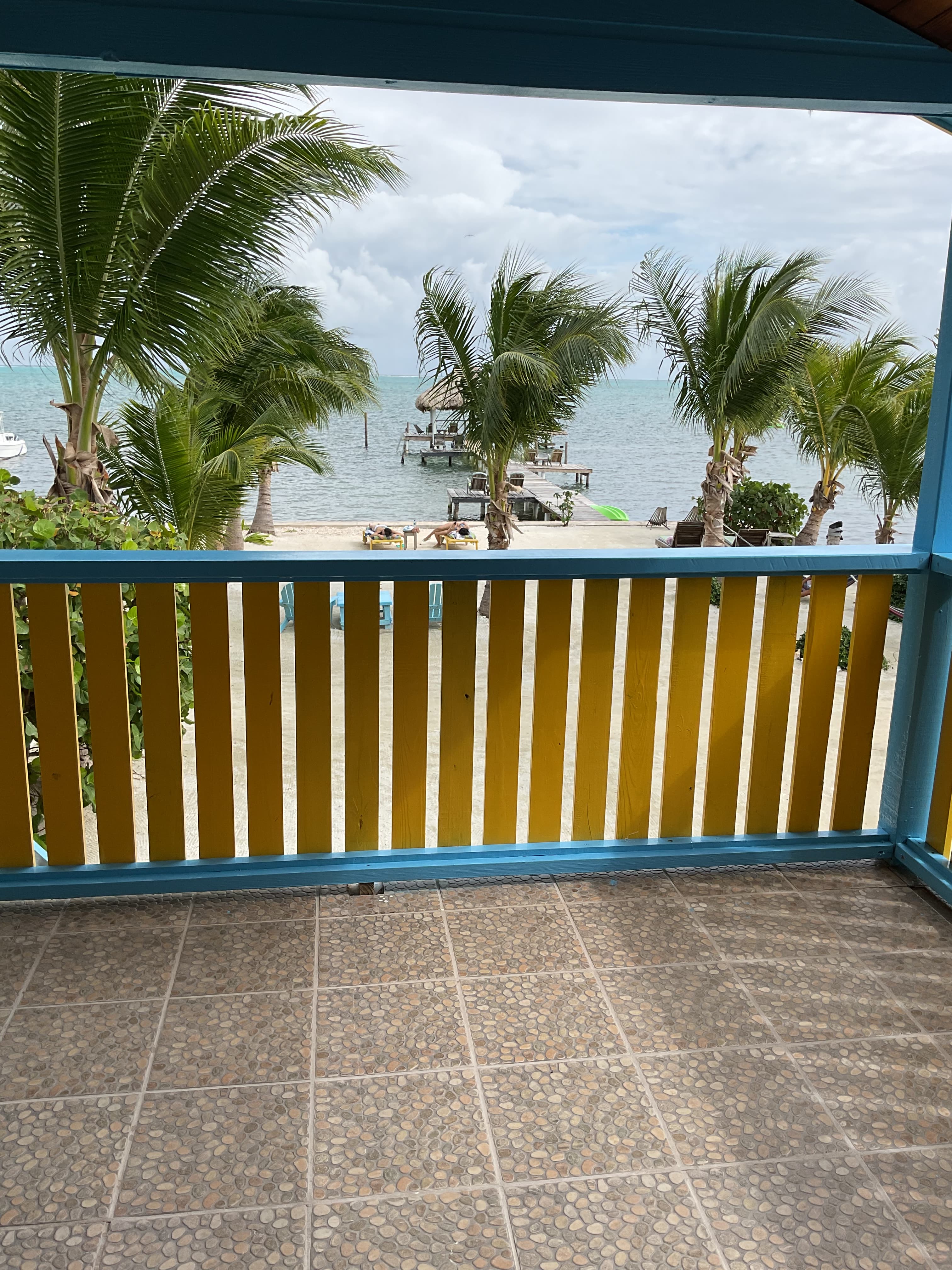 View of a beach with palm trees from a deck, featuring blue and yellow railings.