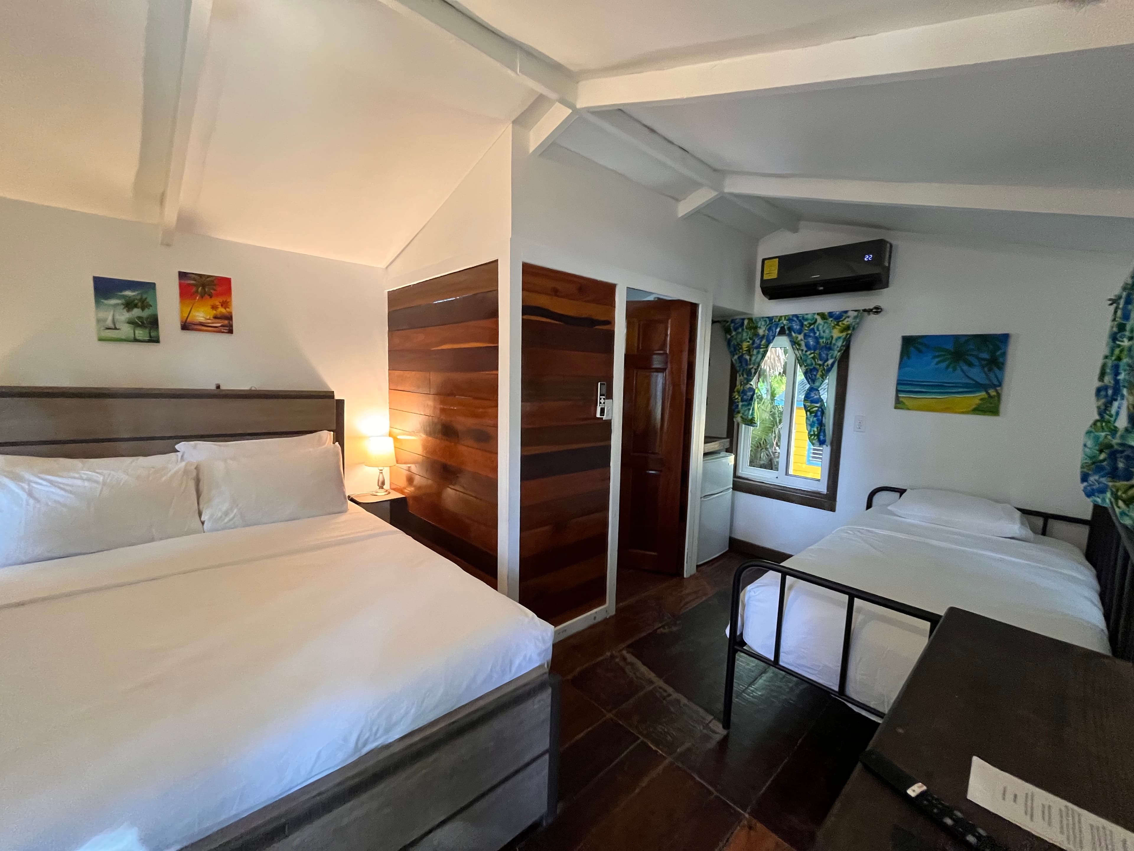 A cozy hotel room featuring a double bed and a single bed, with wooden accents and colorful artwork on the walls.