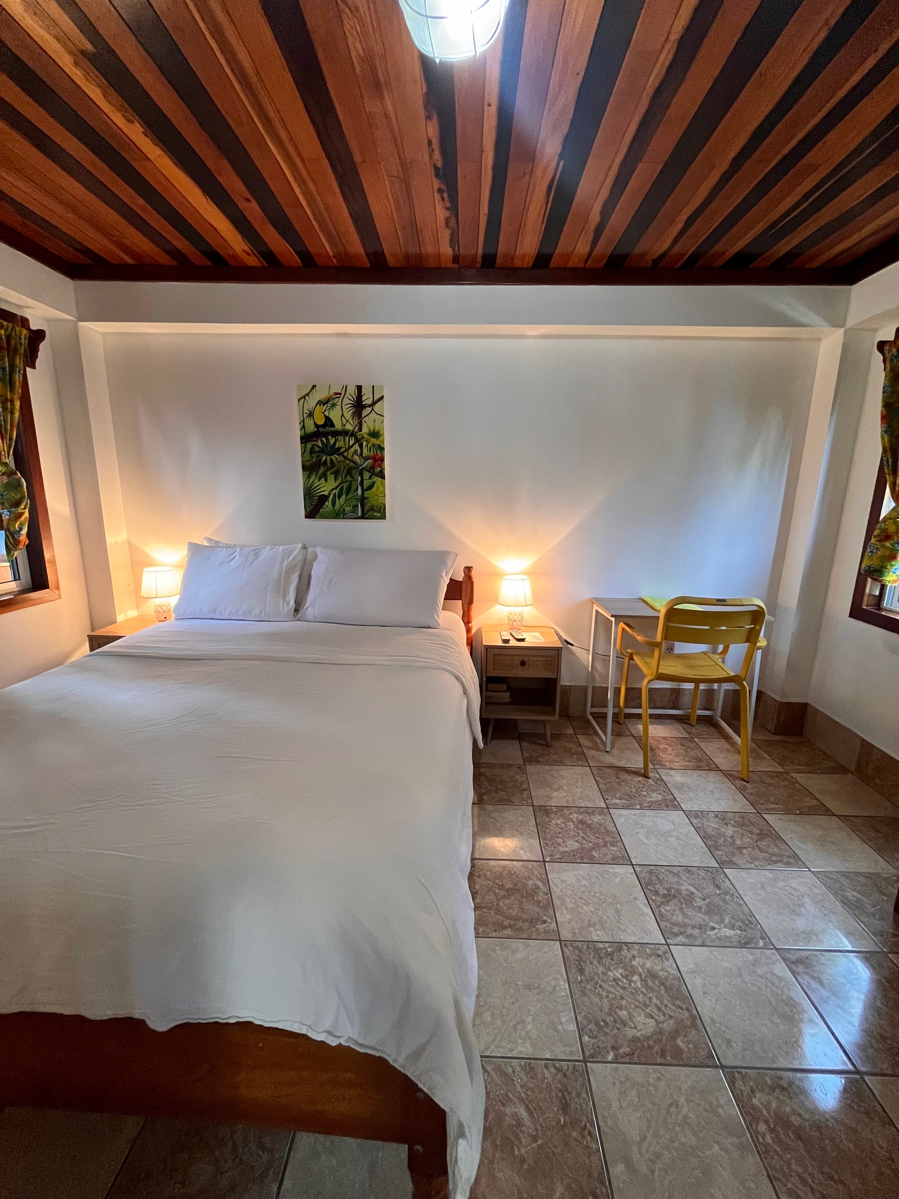 A cozy bedroom featuring a double bed, bedside tables with lamps, and a small workspace.