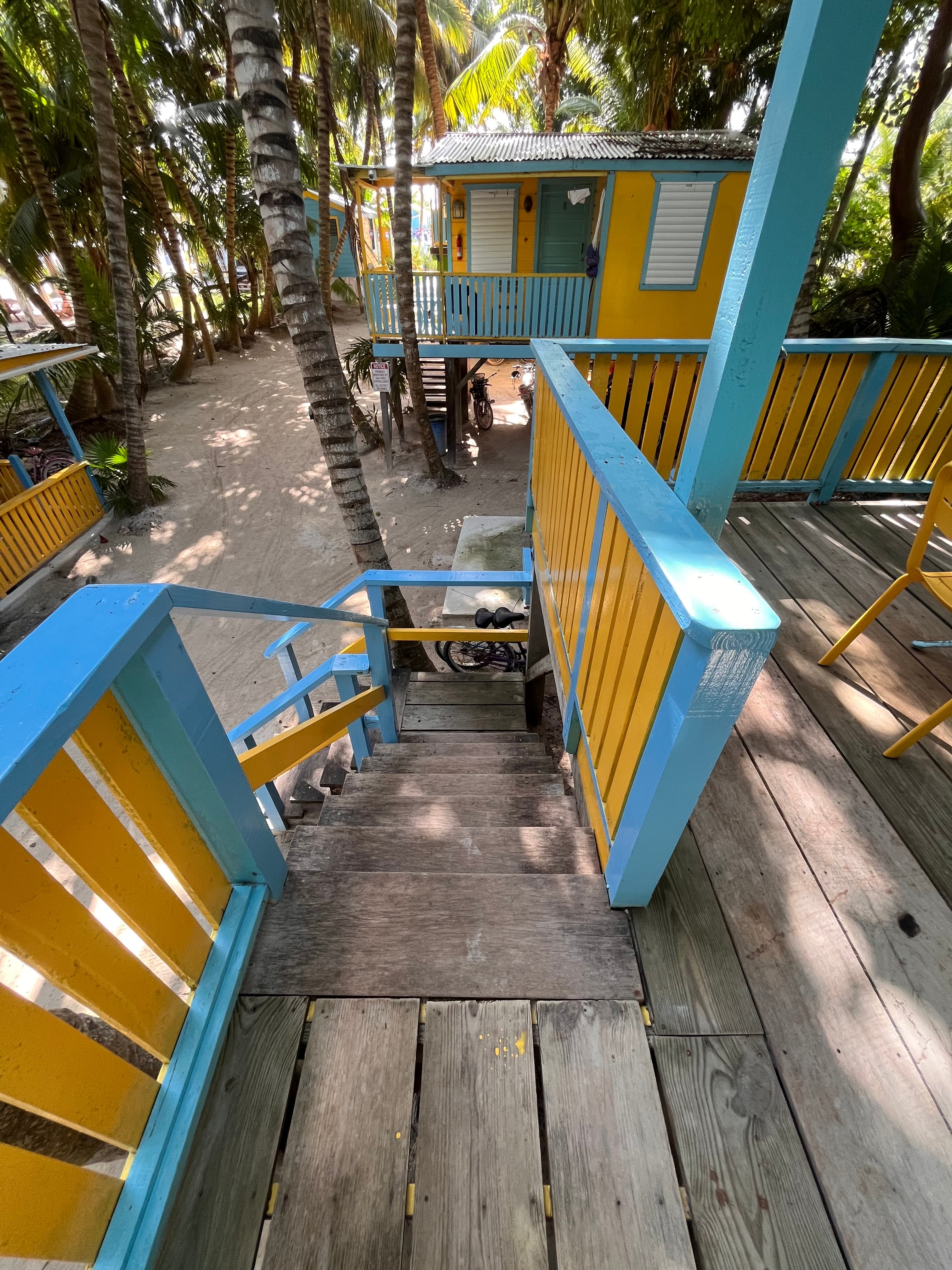A colorful wooden staircase leads down from a platform surrounded by palm trees to a sandy area below.
