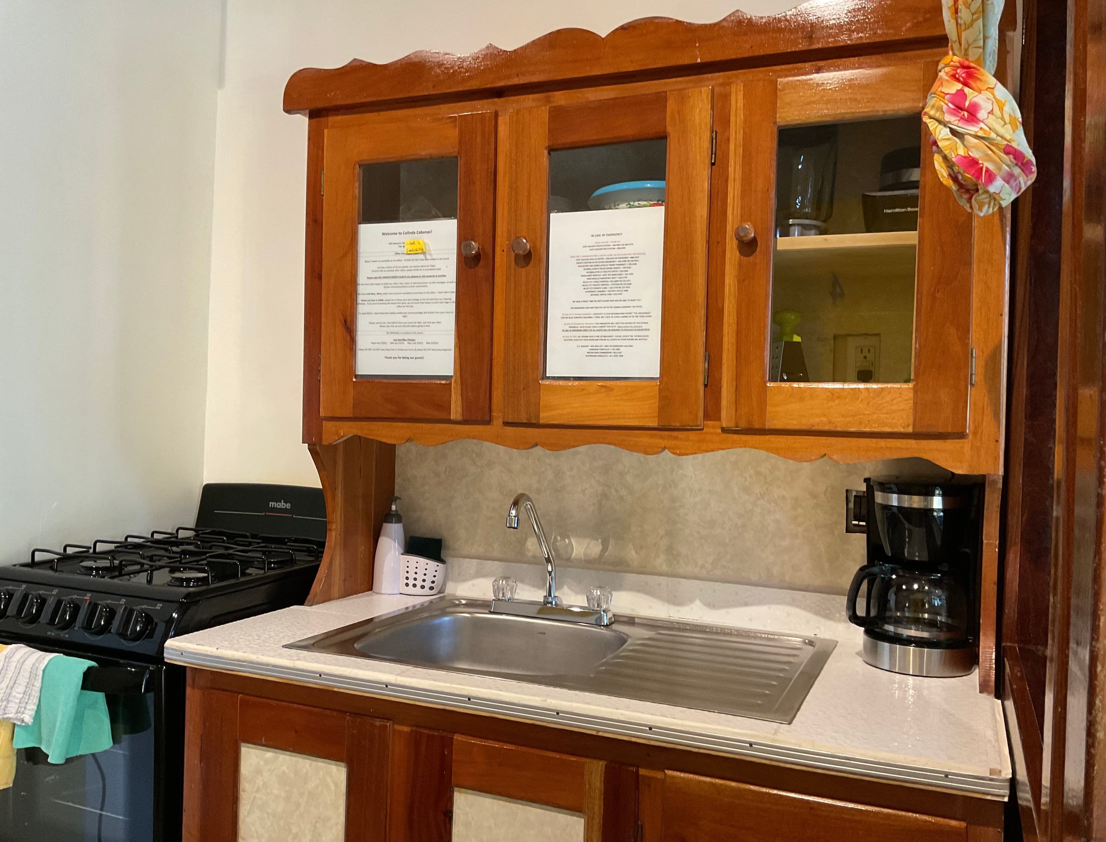 A wooden kitchen cabinet above a stainless steel sink, with a coffee maker and a stove nearby.