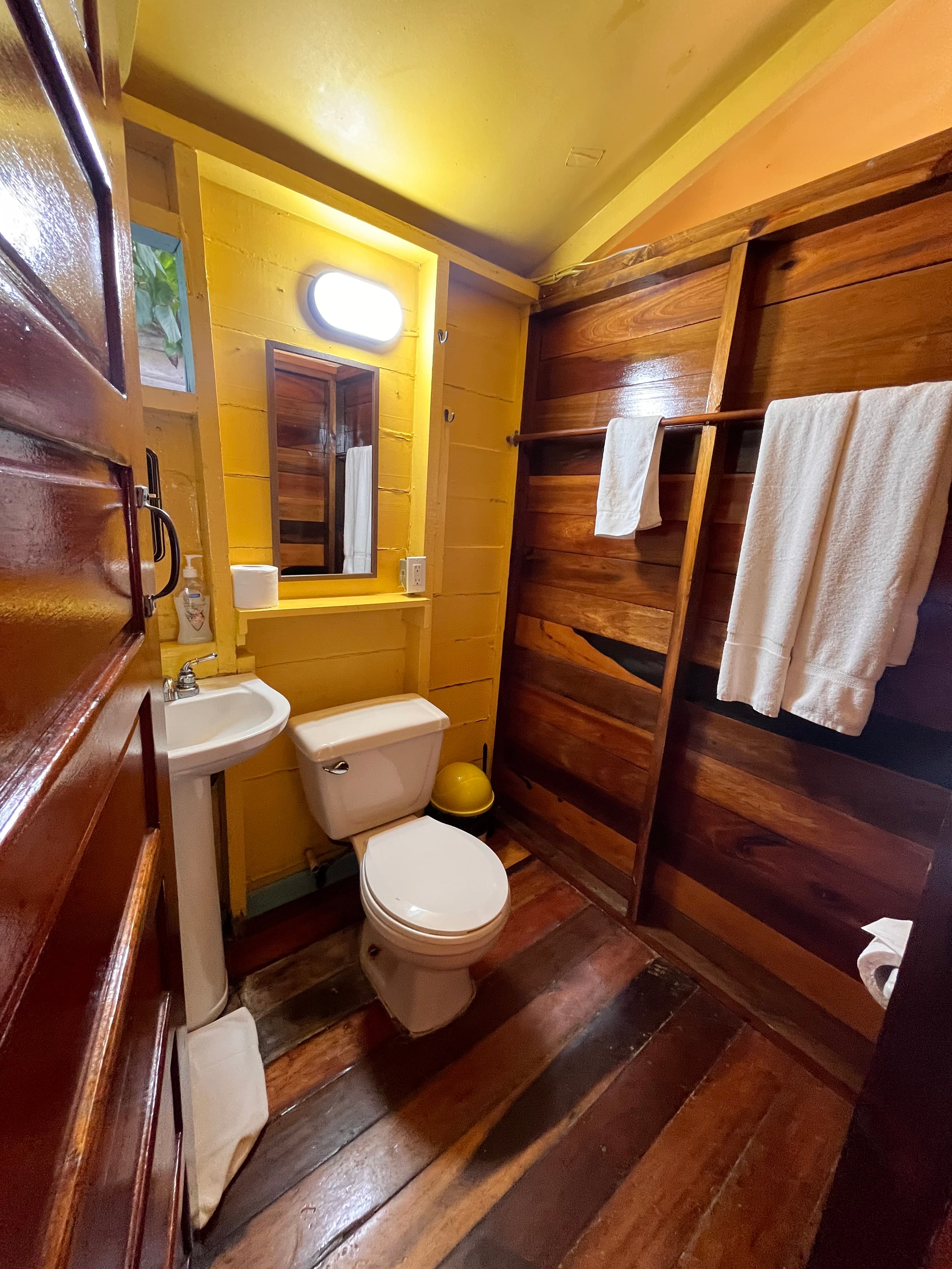 A small bathroom featuring a toilet, sink, mirror, and wooden accents with towels hanging on the wall.
