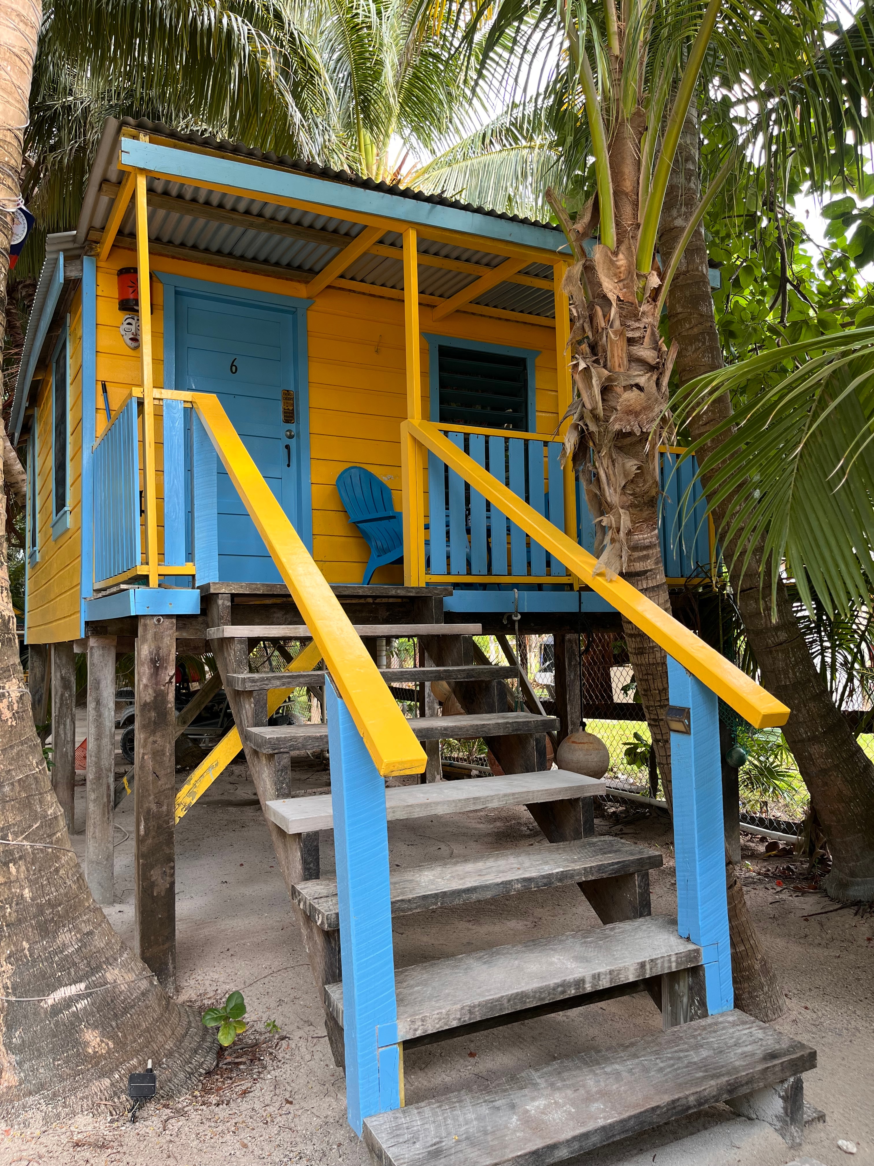 A colorful wooden cabin on stilts surrounded by palm trees.