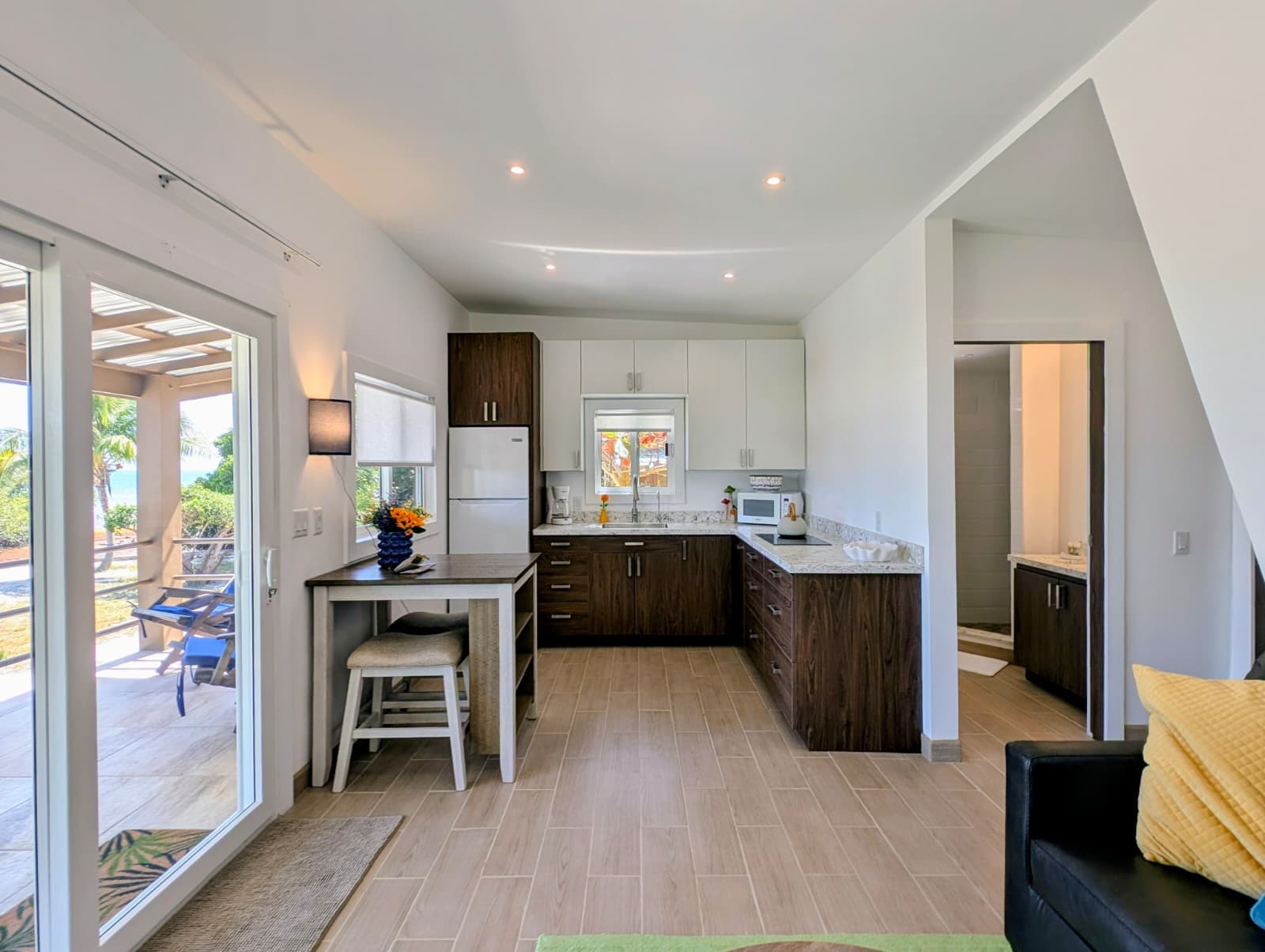 Modern kitchen with wooden cabinets and a dining area, featuring natural light and a door leading to an outdoor patio.