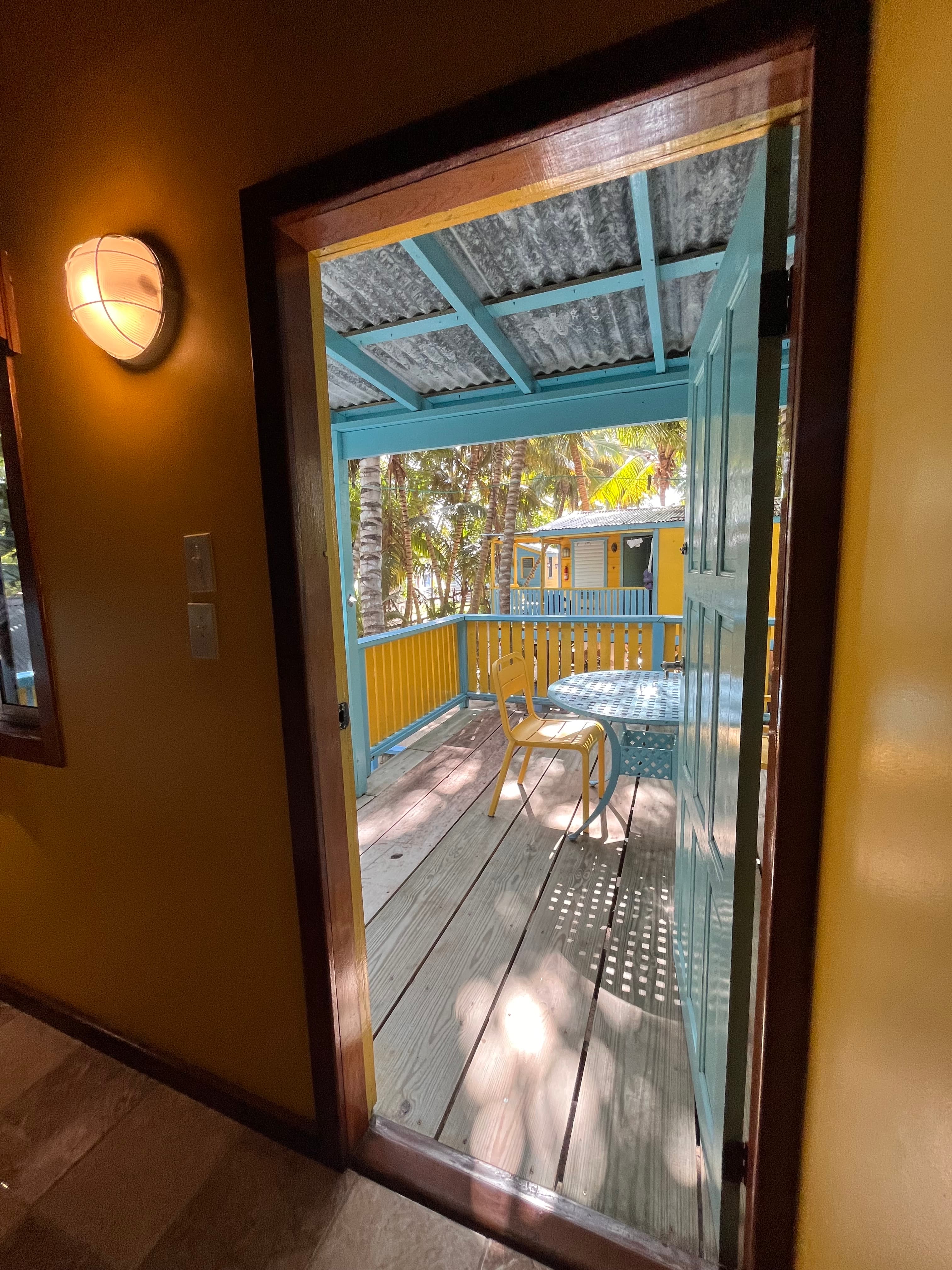 View of a sunny outdoor patio through an open doorway with a yellow wall.