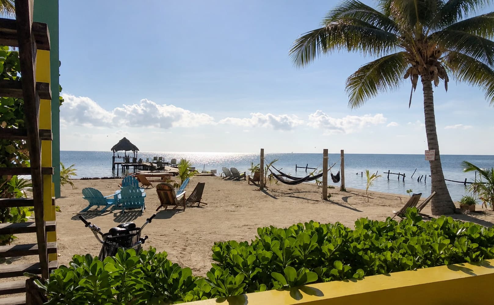 A serene beach scene featuring sun loungers, hammocks, and a distant pier under a bright sky.