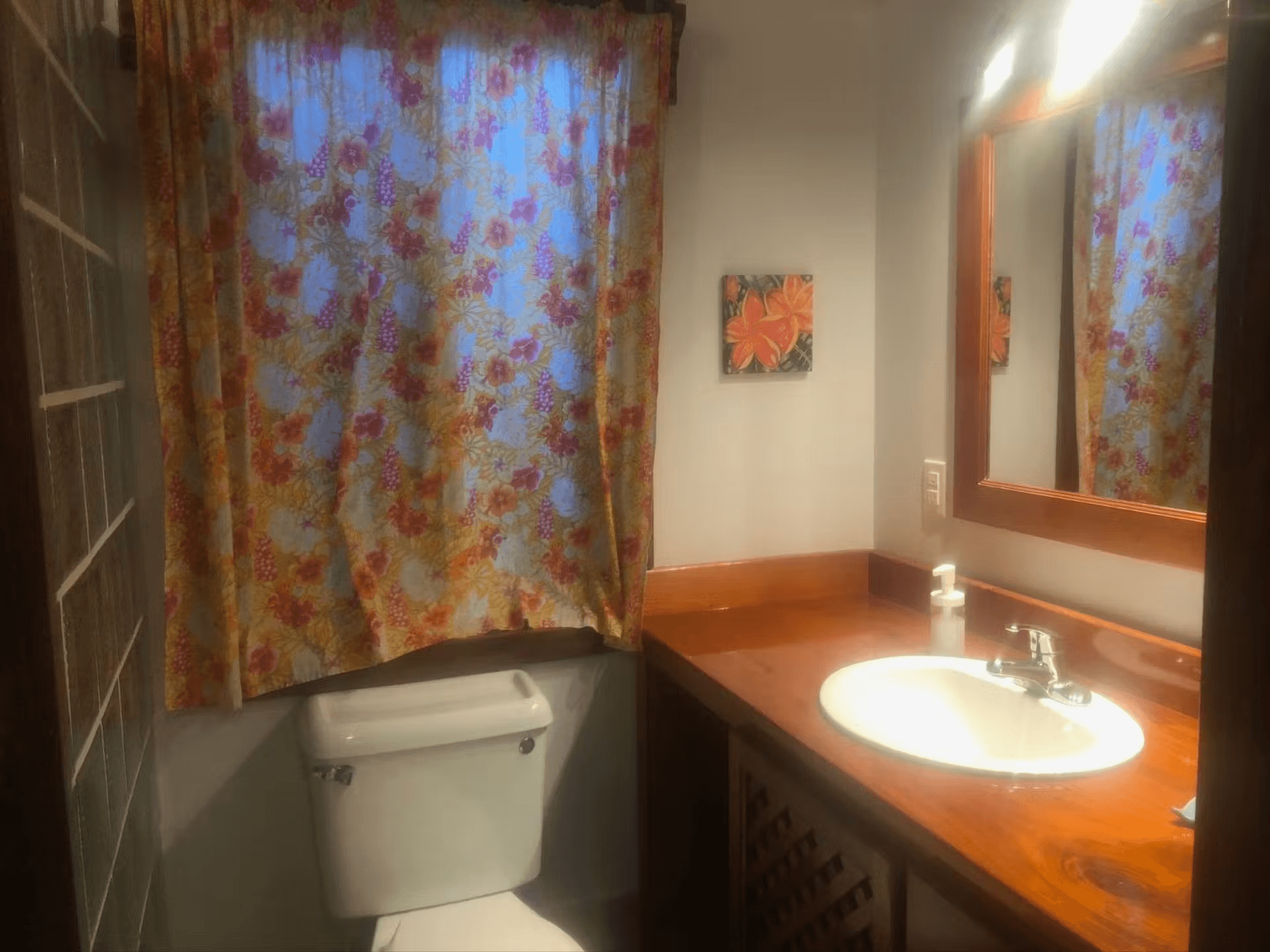 Bathroom with beautiful hardwood vanity, gleaming white sink, and toilet with curtained window above