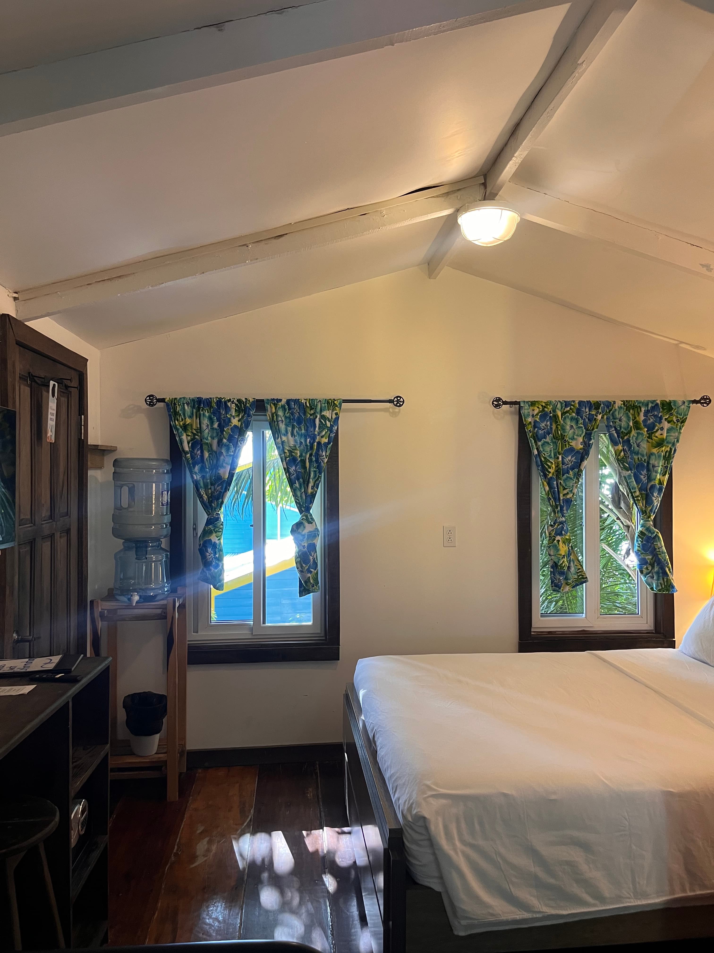 Bright and airy bedroom featuring floral curtains, a water cooler, and natural light streaming through the windows.