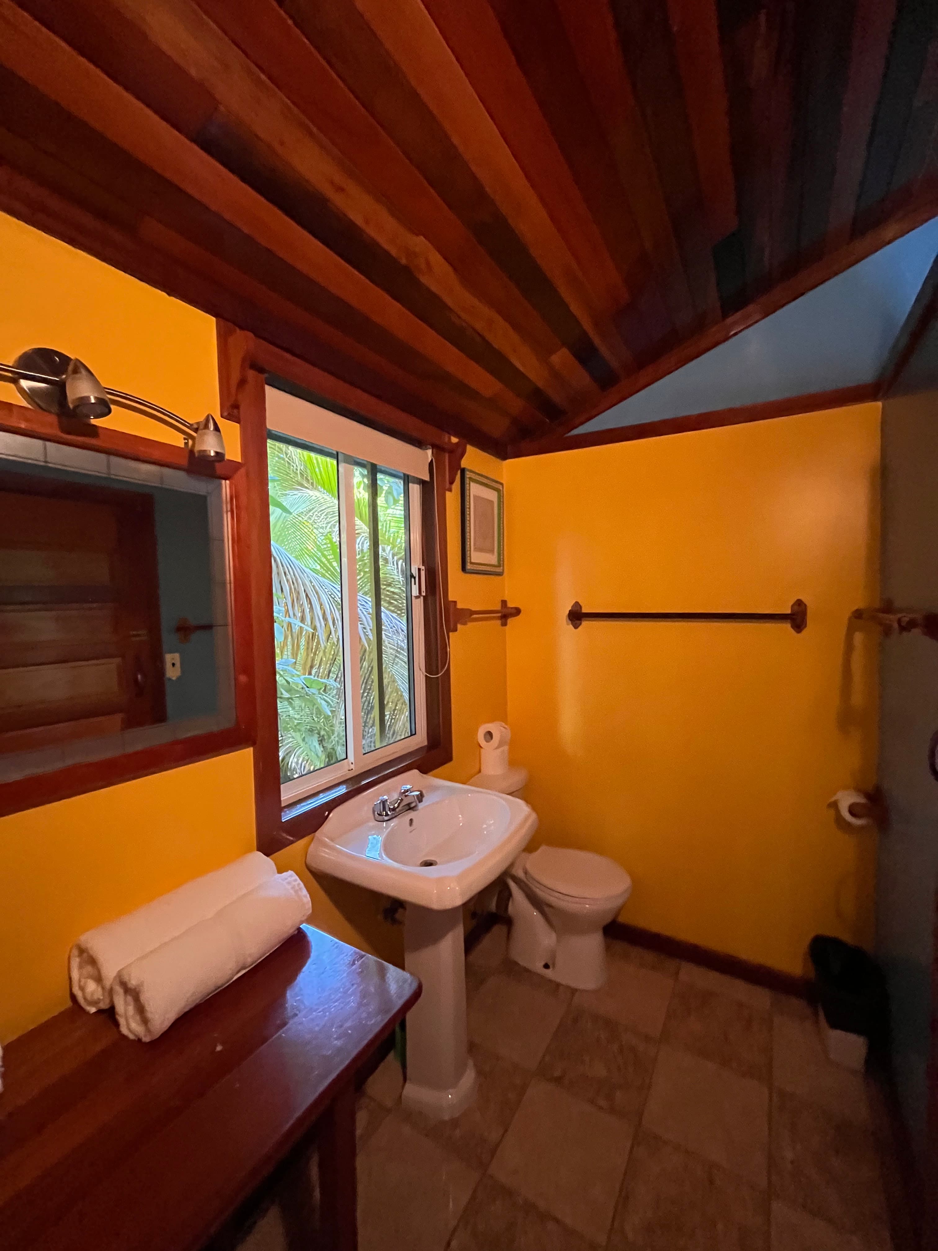 A bright yellow bathroom featuring a sink, toilet, and window with a view of foliage.