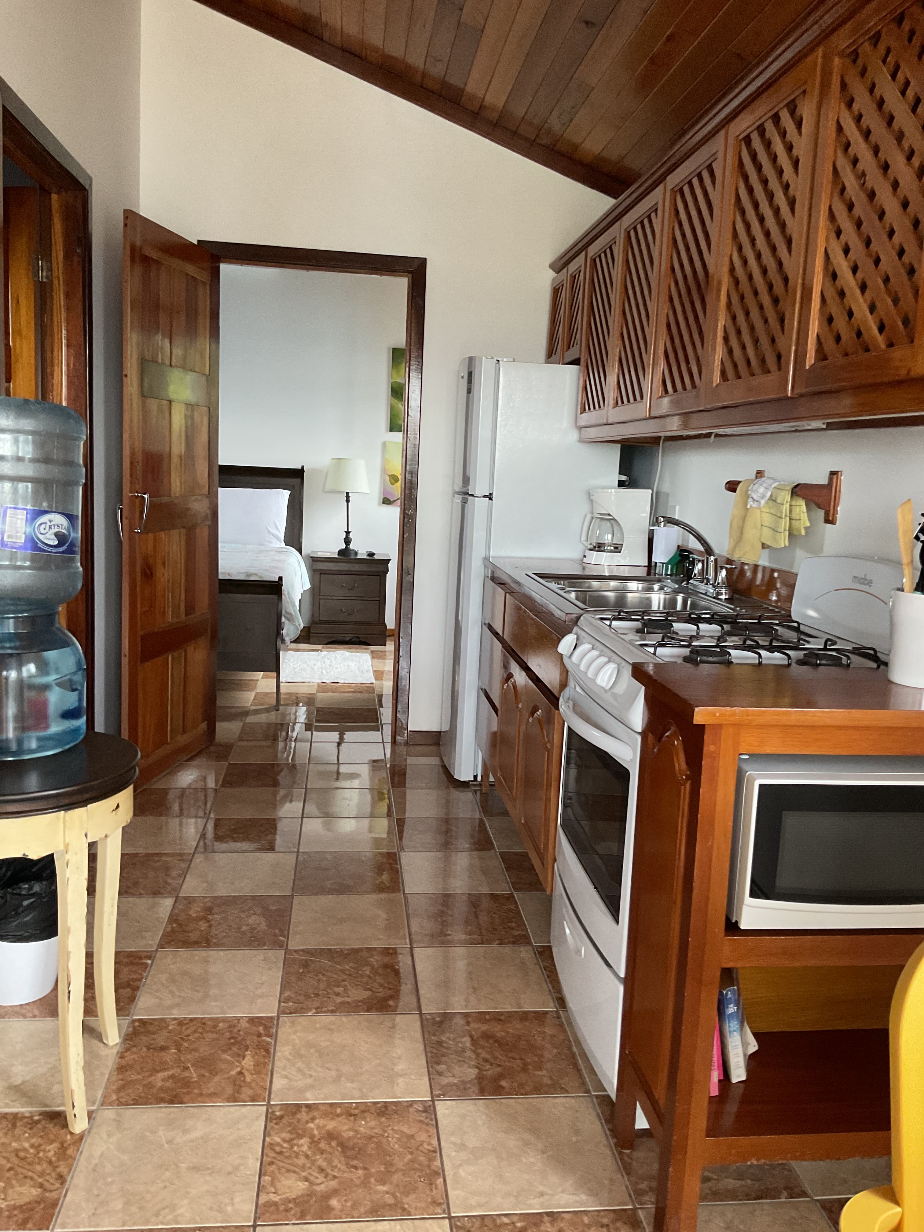 A view of a kitchen with wooden cabinetry, tiled floor, and an open doorway leading to a bedroom.