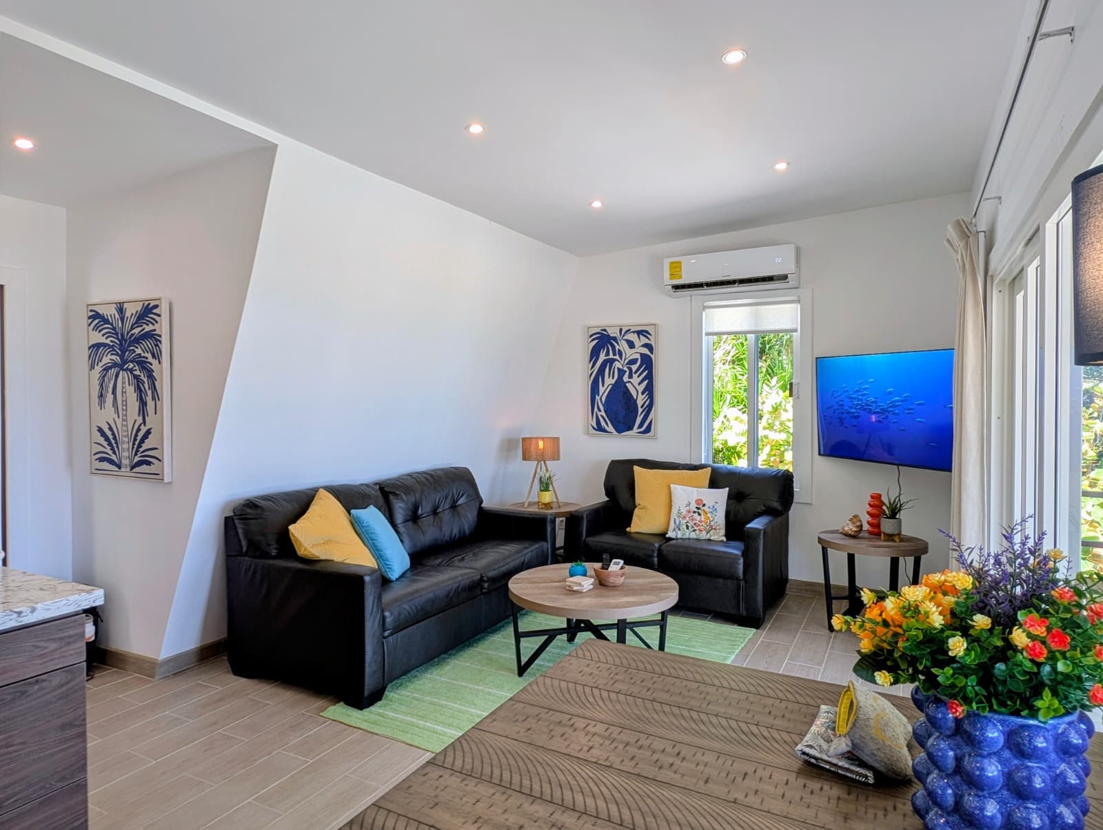 Bright, modern living room with leather sofas, decorative art, and a view of greenery through the window.