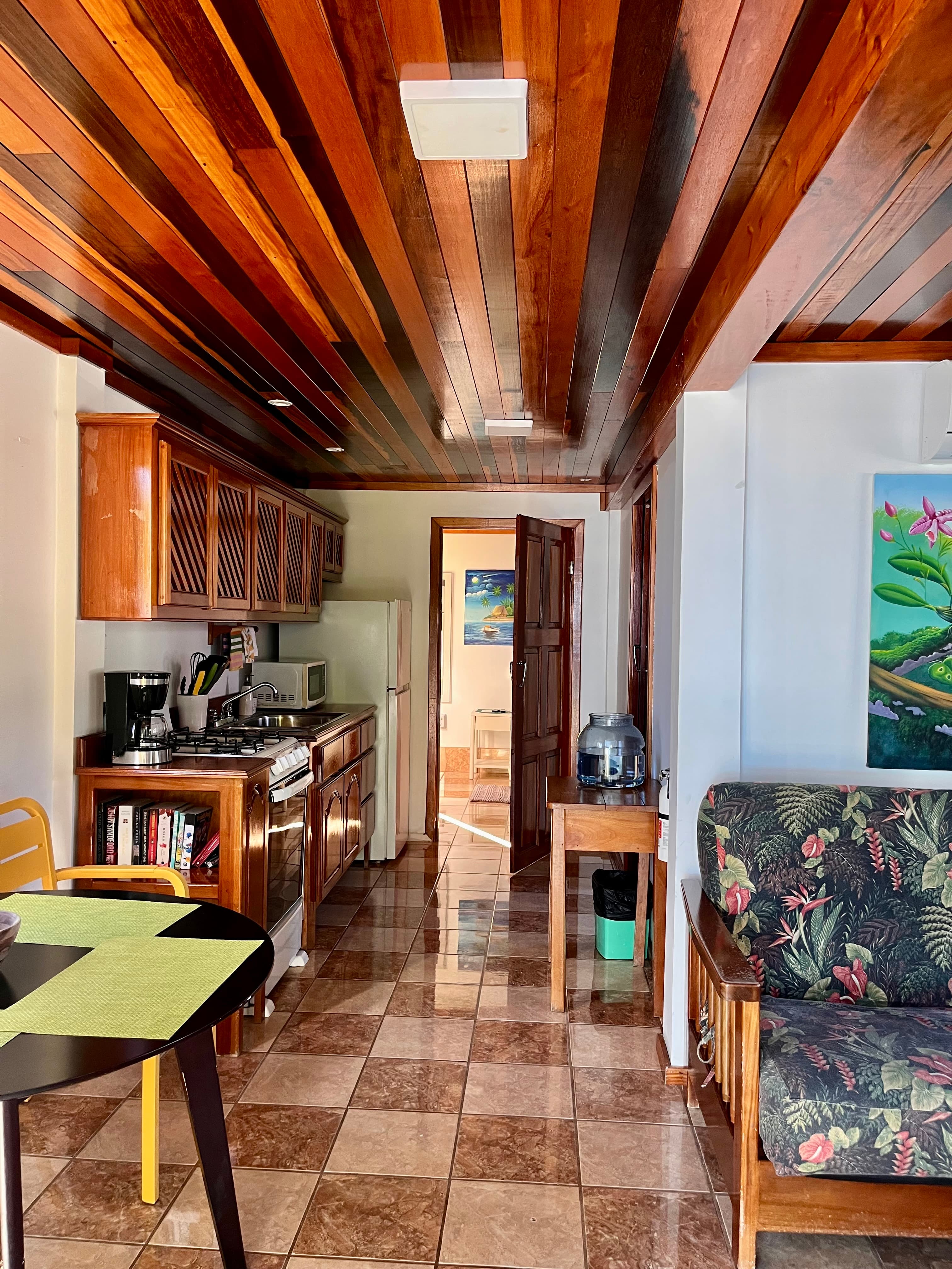 A cozy kitchen and living area with wooden cabinets, tiled floors, and a floral-patterned couch.