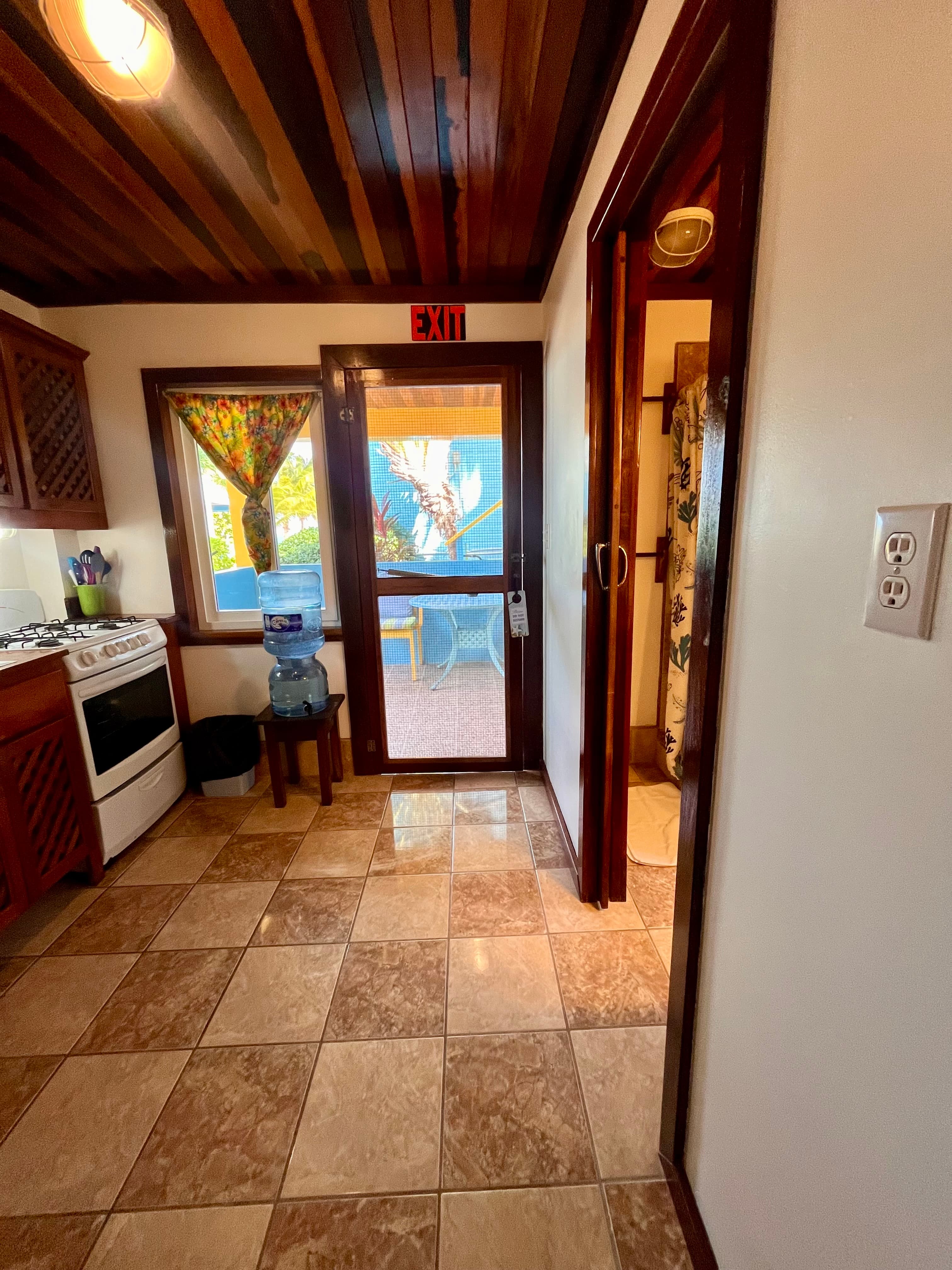 A bright kitchen entrance with a water cooler, tiled floors, and a door leading outside.