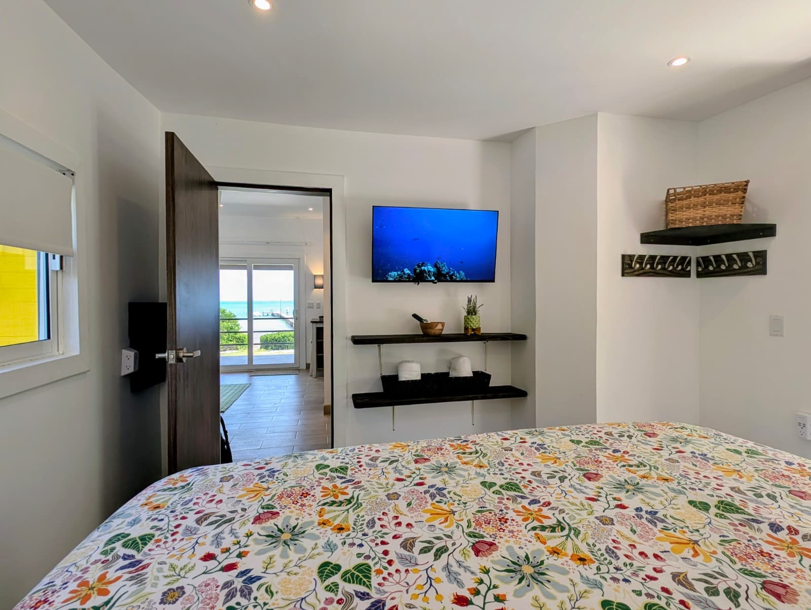 A brightly decorated bedroom featuring a floral bedspread, a TV mounted on the wall, and a door leading to an outdoor view.