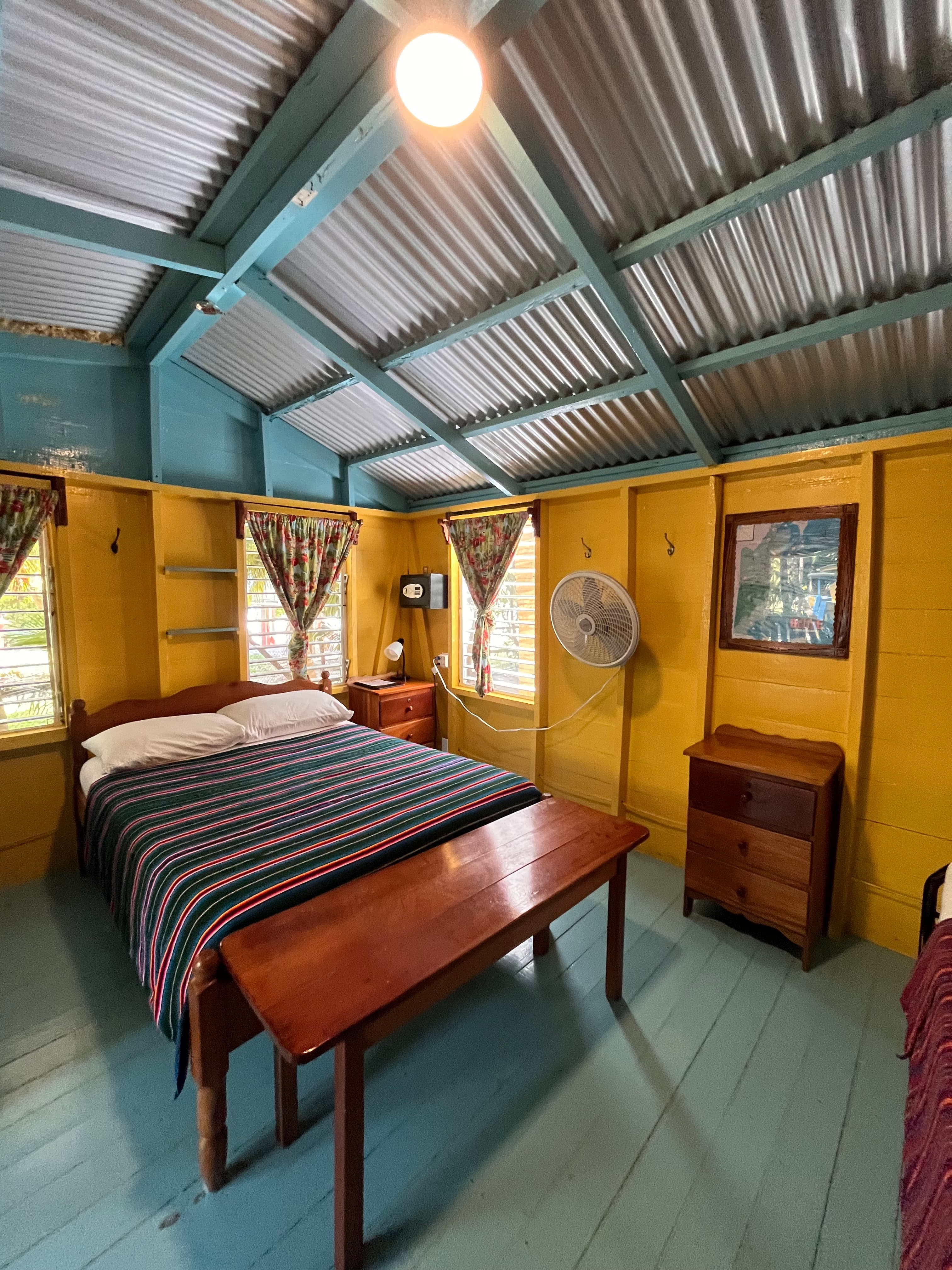 A colorful and cozy bedroom featuring a double bed, wooden furniture, and vibrant walls.