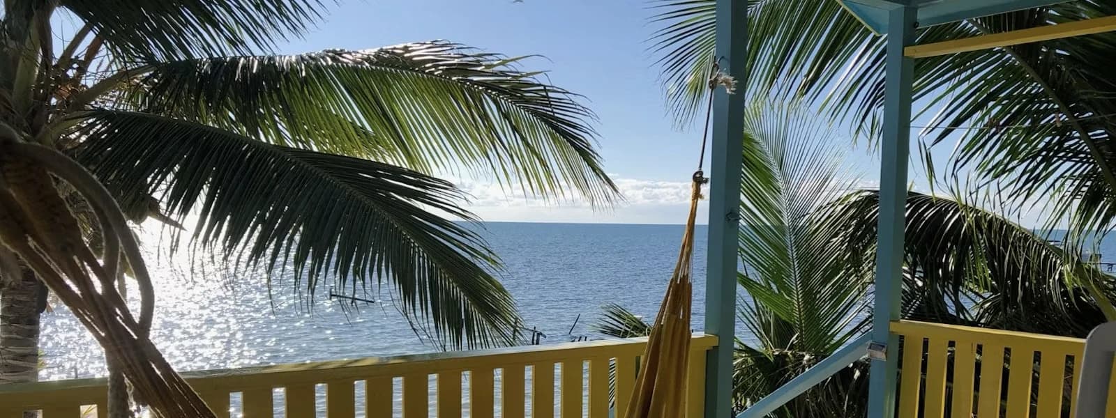 View of calm ocean waters framed by palm trees and a colorful balcony railing.