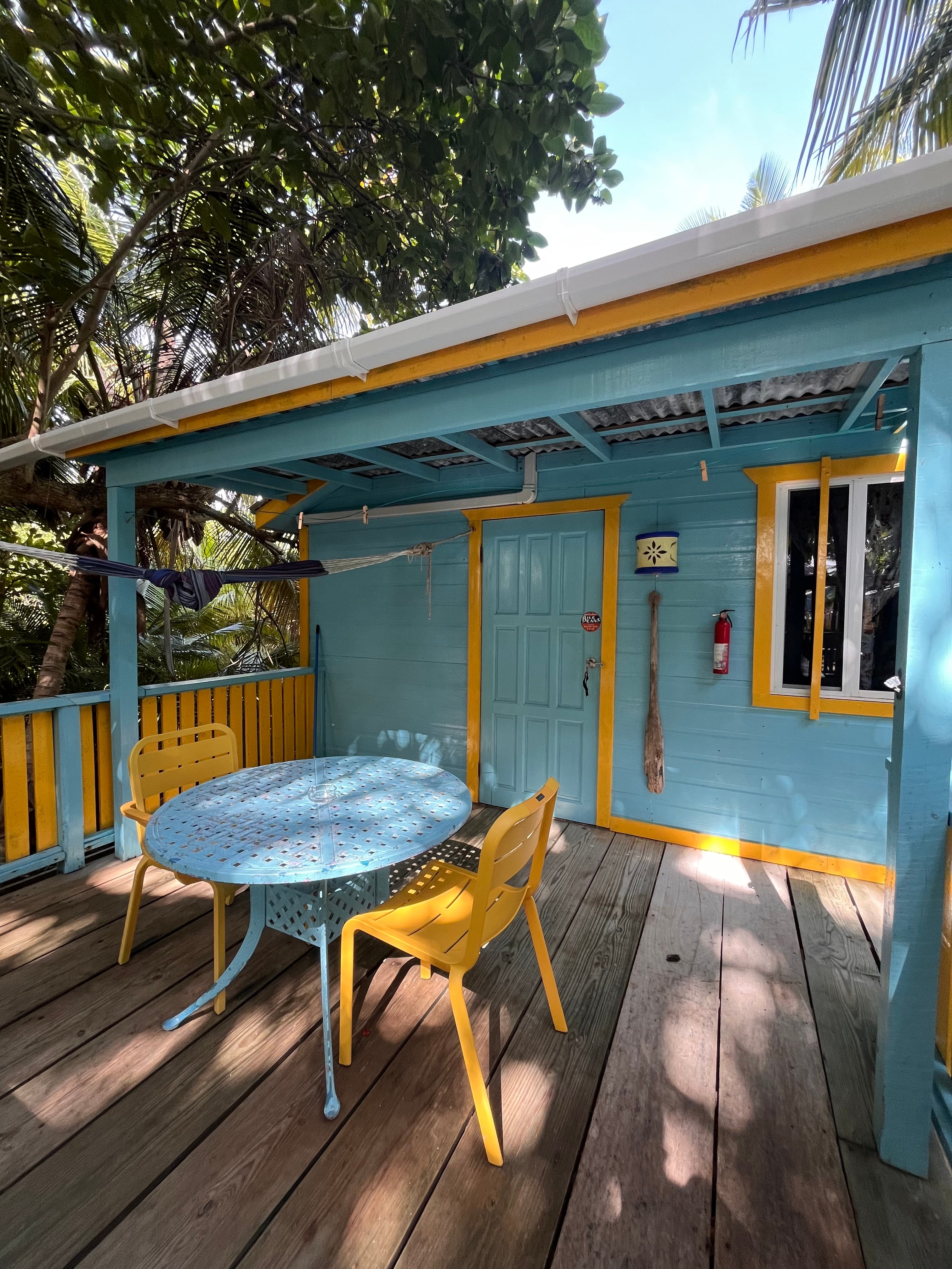 Colorful coastal cottage with a blue and yellow exterior, featuring a round table and chairs on a wooden deck.