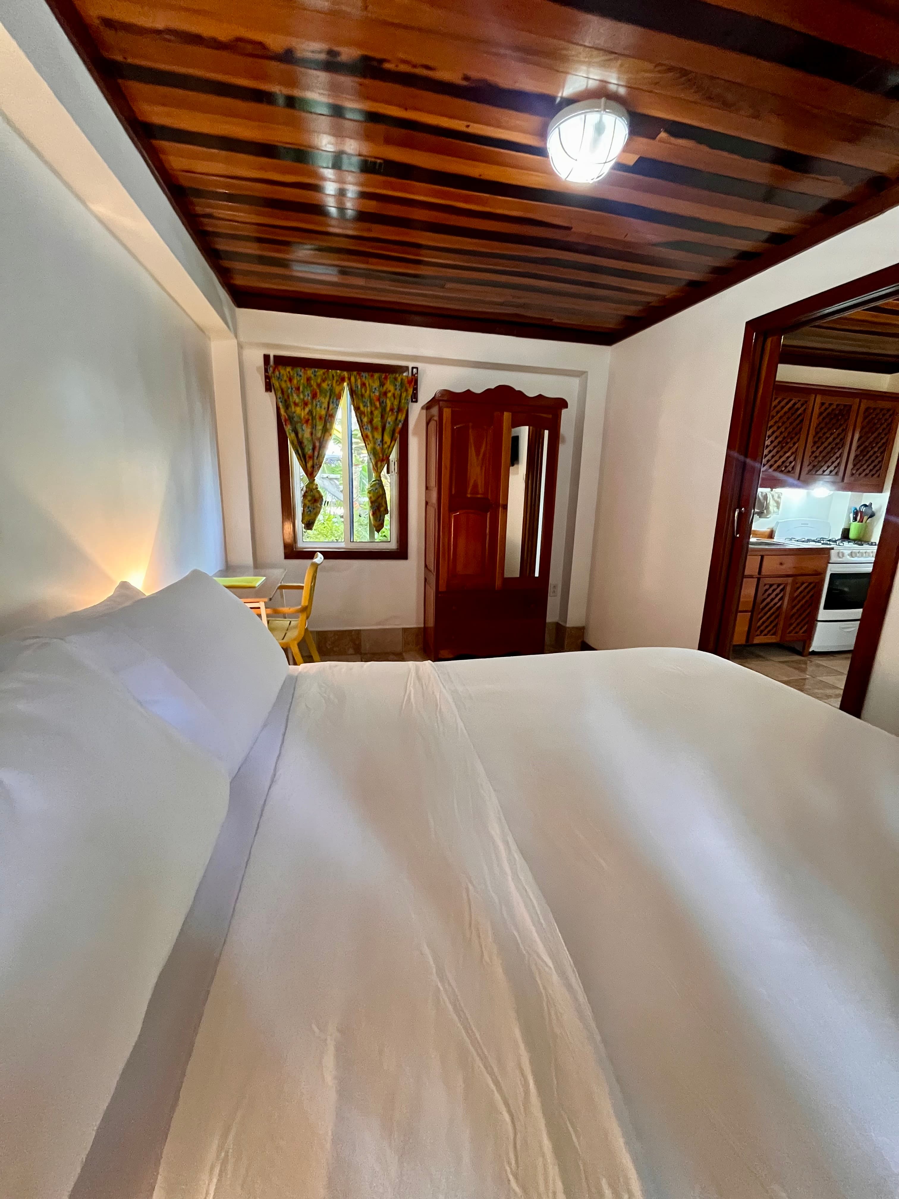 A cozy bedroom with a large bed, wooden beams, and a window adorned with colorful curtains.