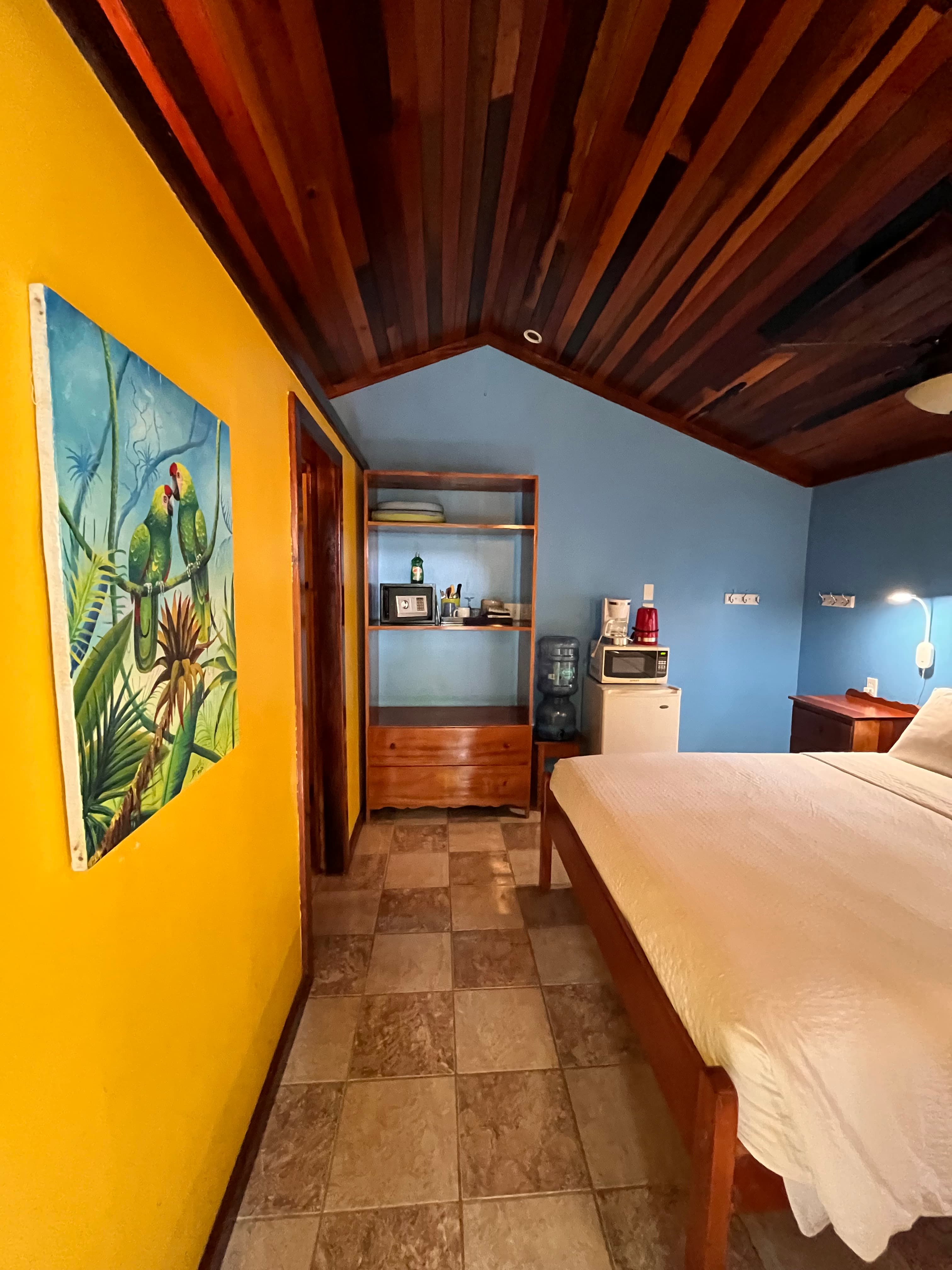 A cozy bedroom with yellow and blue walls, a wooden ceiling, and a painting of two parrots.