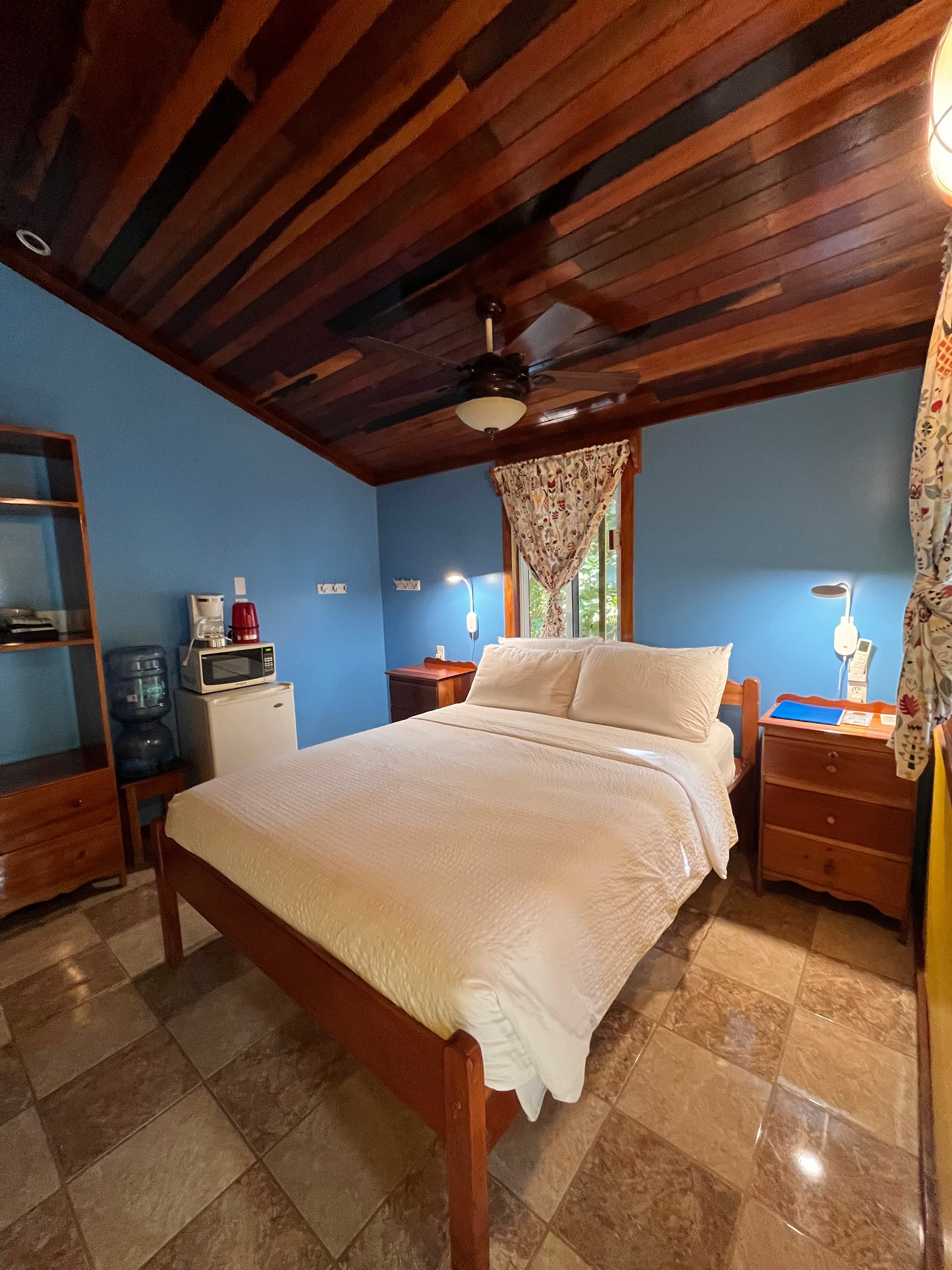 A cozy bedroom featuring a wooden bed, blue walls, and natural light from a window.