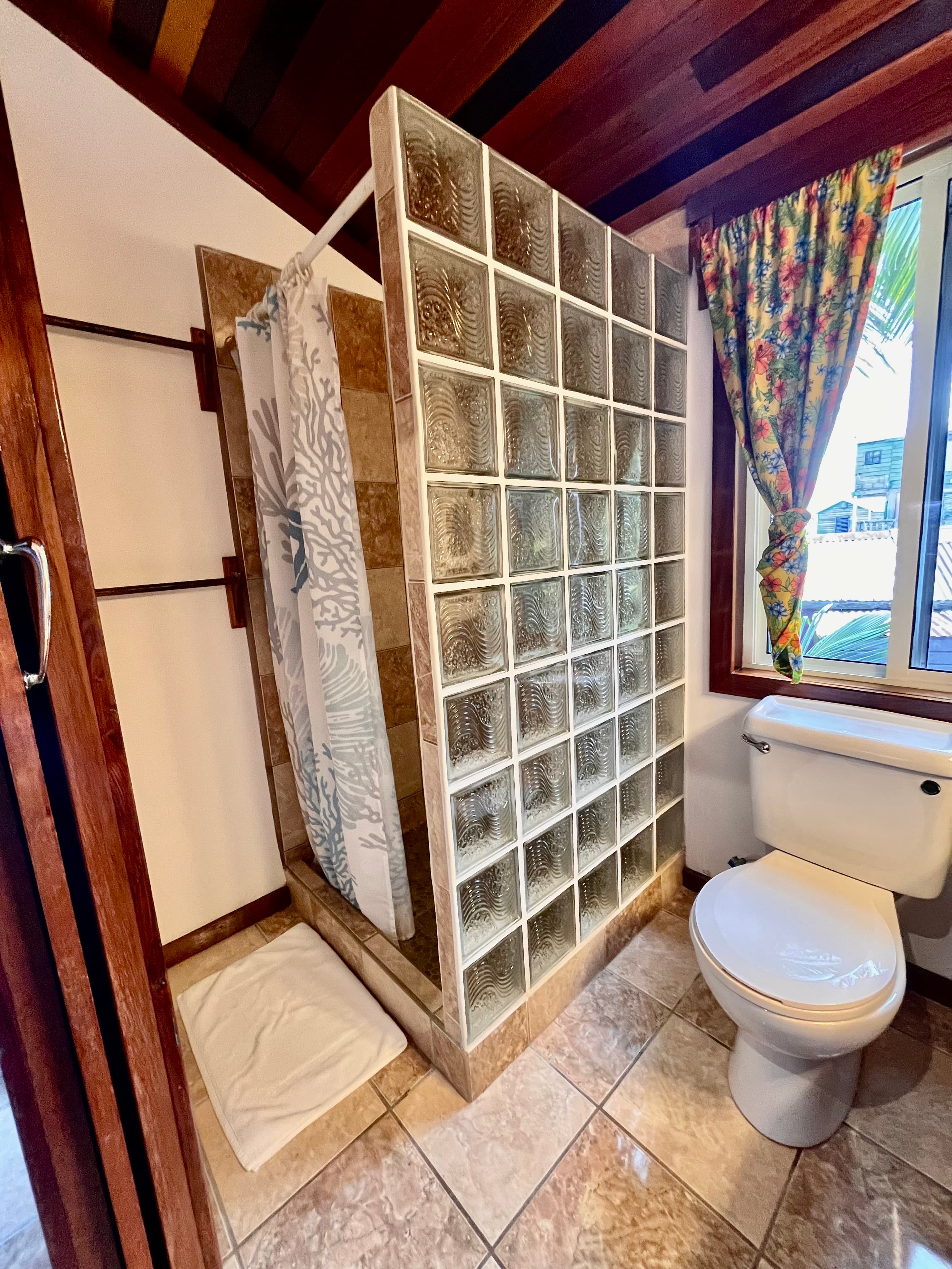 A modern bathroom featuring a glass block shower, toilet, and colorful floral window curtain.