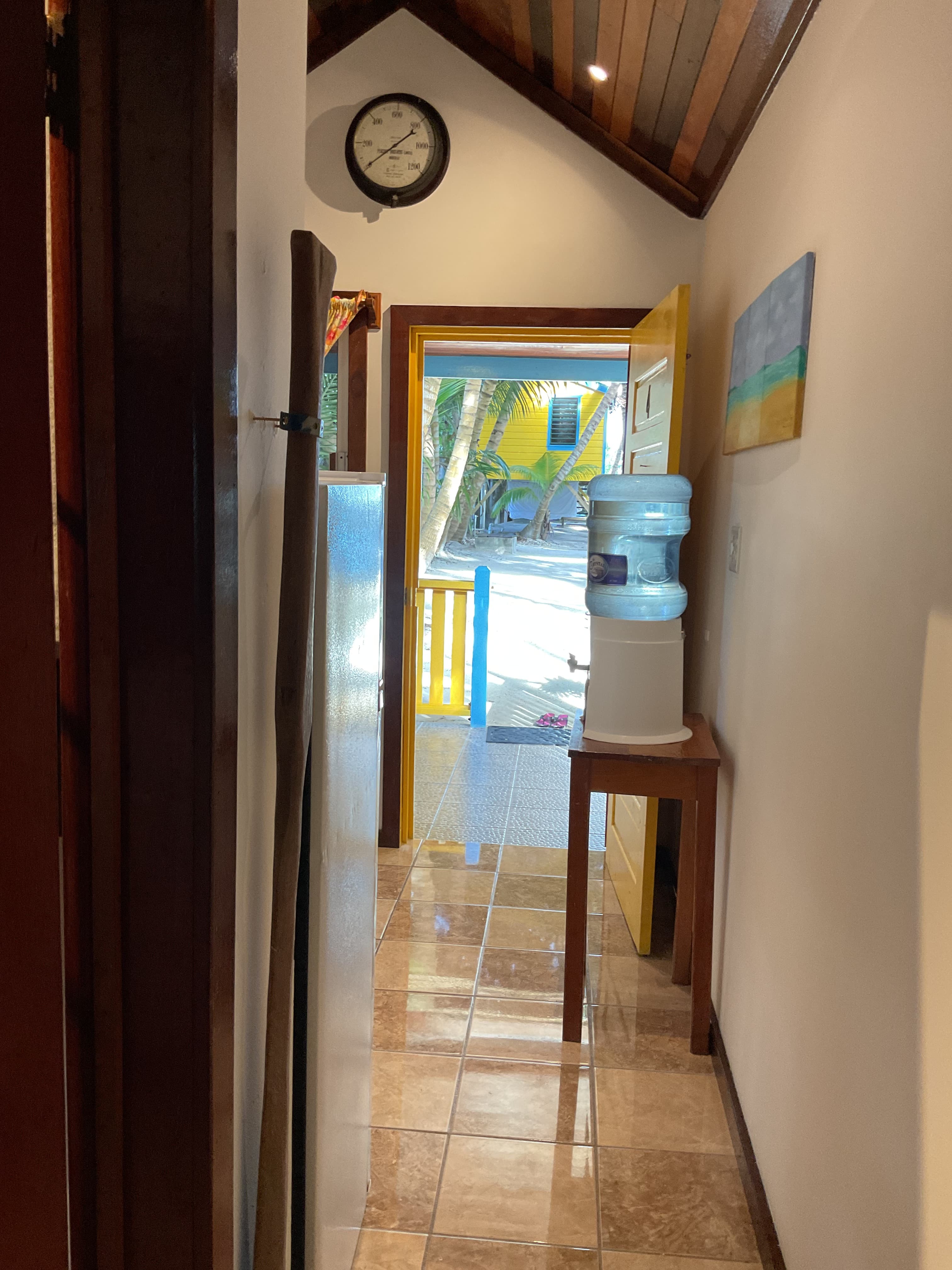 A hallway leading to an open door with a water cooler on a wooden table.
