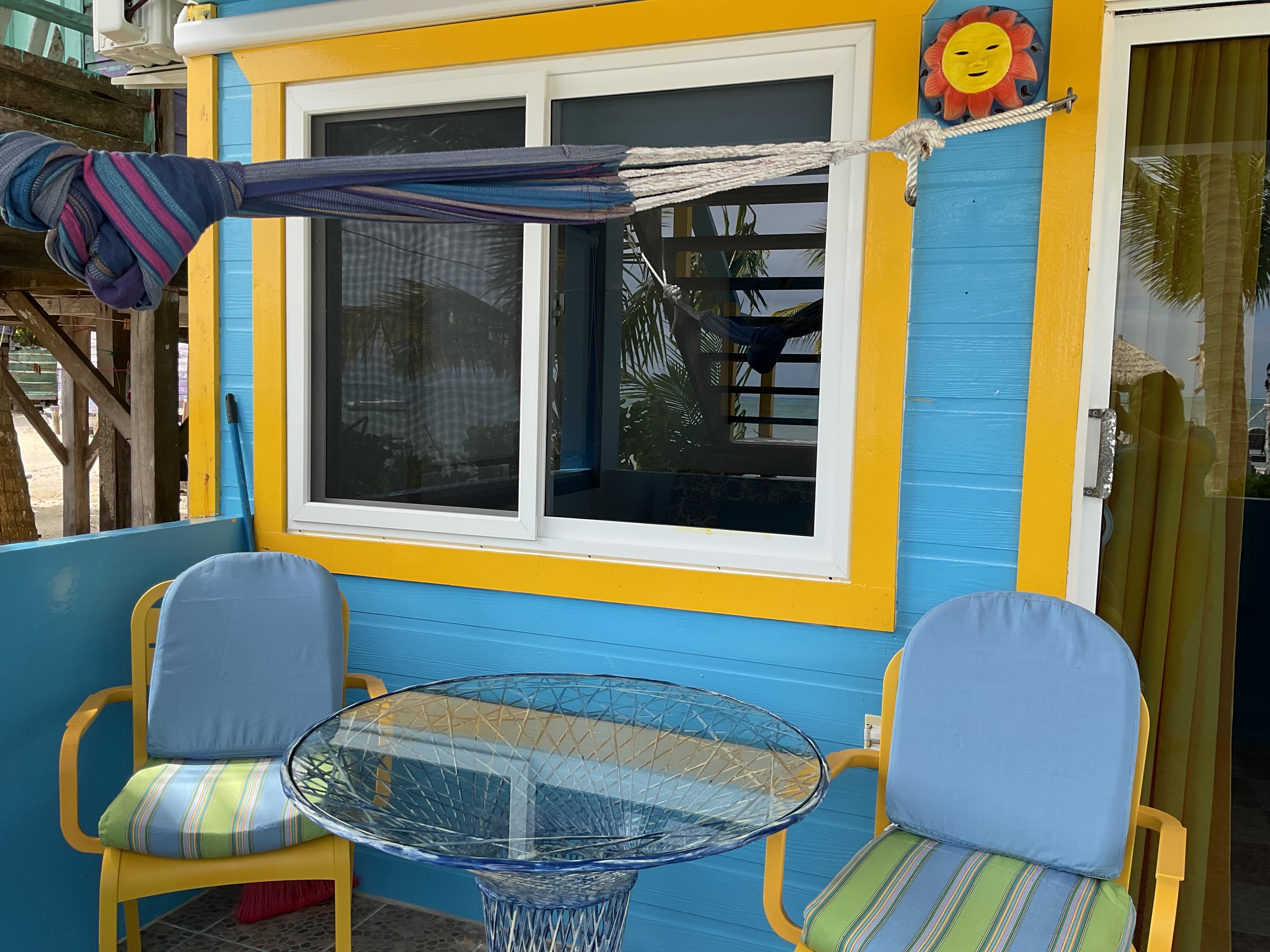 Colorful outdoor seating area with two chairs and a glass table beside a bright blue and yellow house.