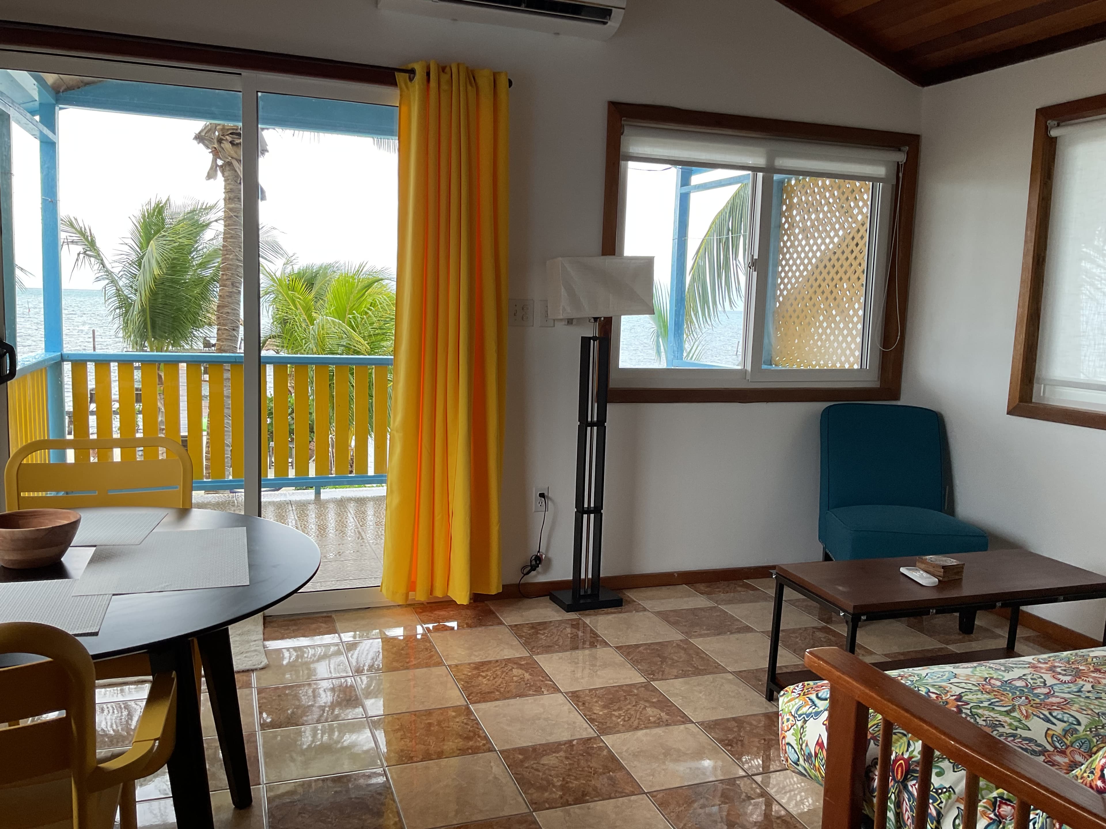 Brightly lit living area with a view of palm trees, featuring a table, chairs, and a cozy seating area.