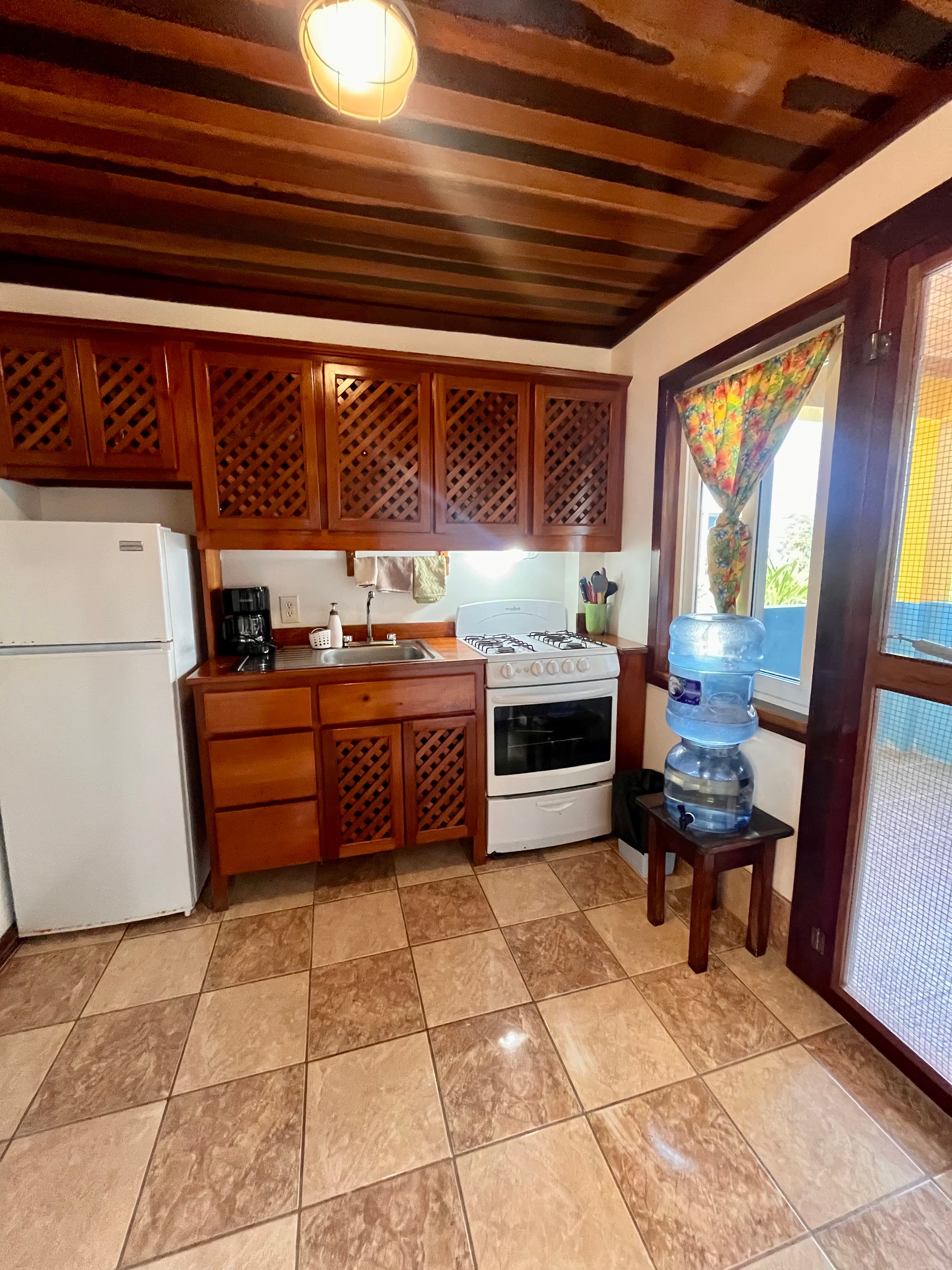 A bright kitchen featuring wooden cabinets, a gas stove, a refrigerator, and a water cooler beside a window.